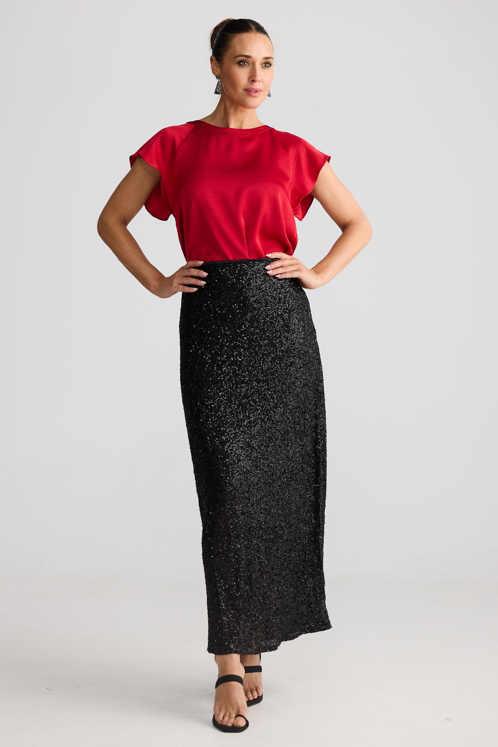 Woman wearing a red top and black sequin skirt on a white background