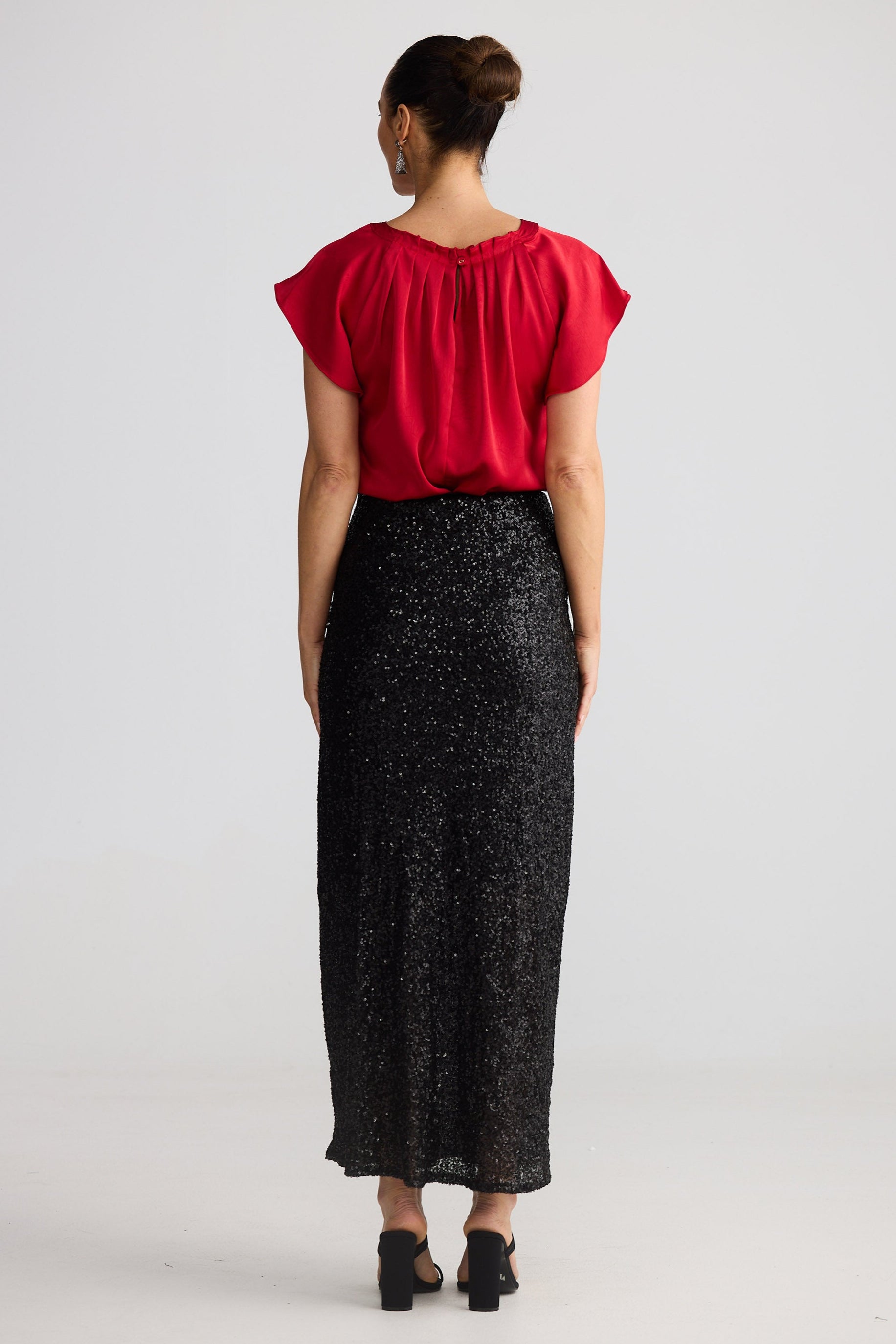 Woman wearing a red top and black sequin skirt on a white background