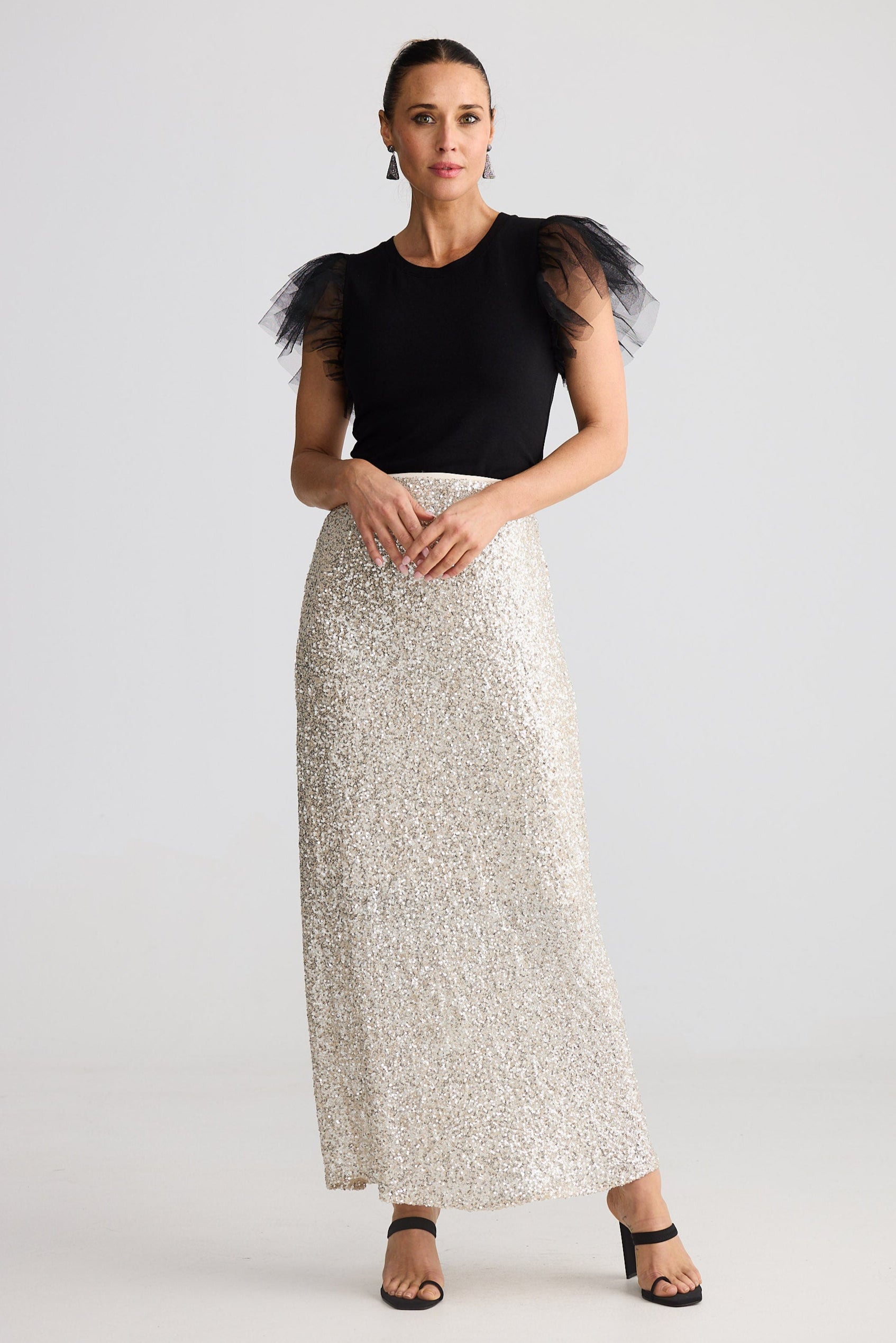 Woman wearing a black top with tulle sleeves and a silver sequin skirt on a white background