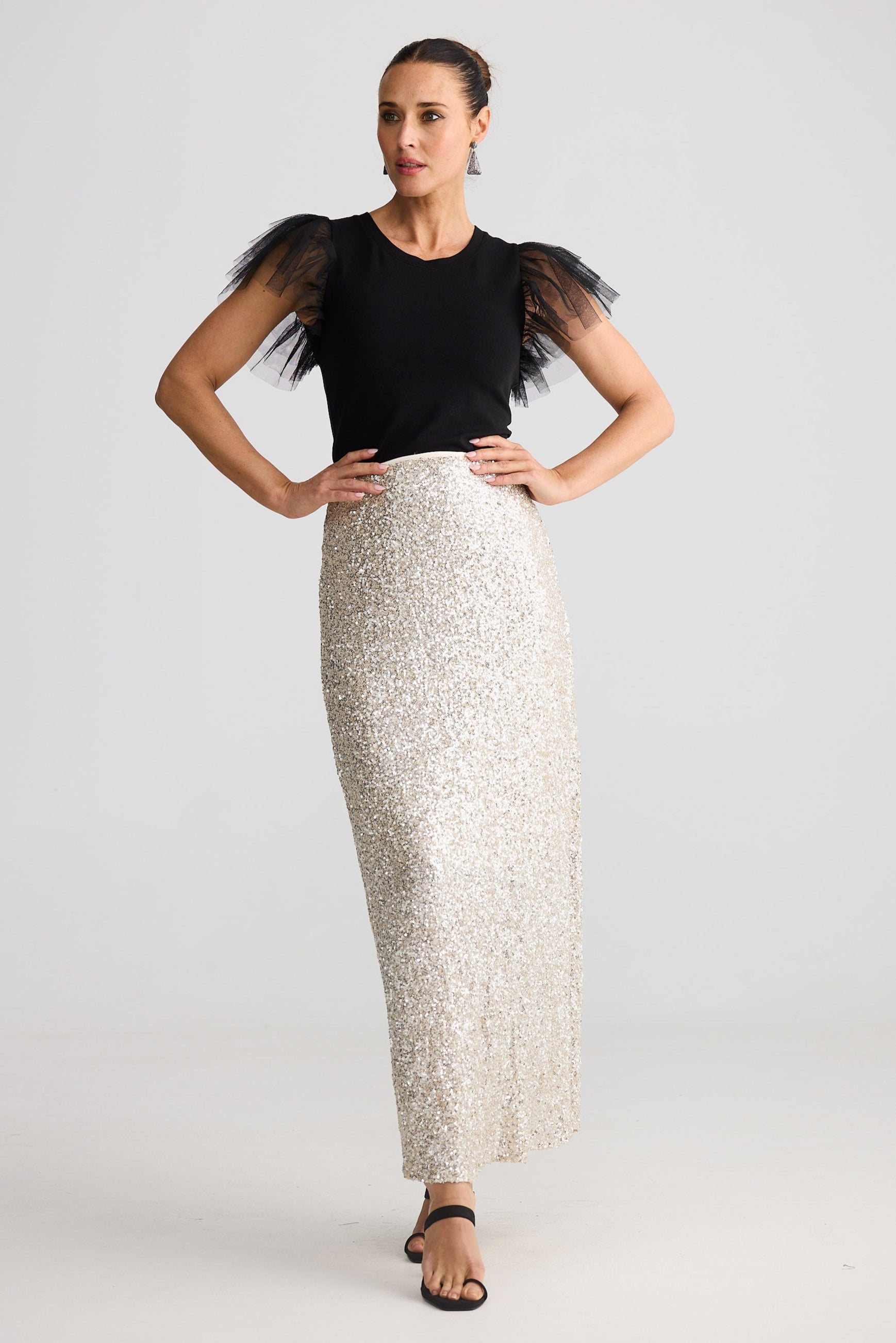 Woman wearing a black top with tulle sleeves and a silver sequin skirt on a white background