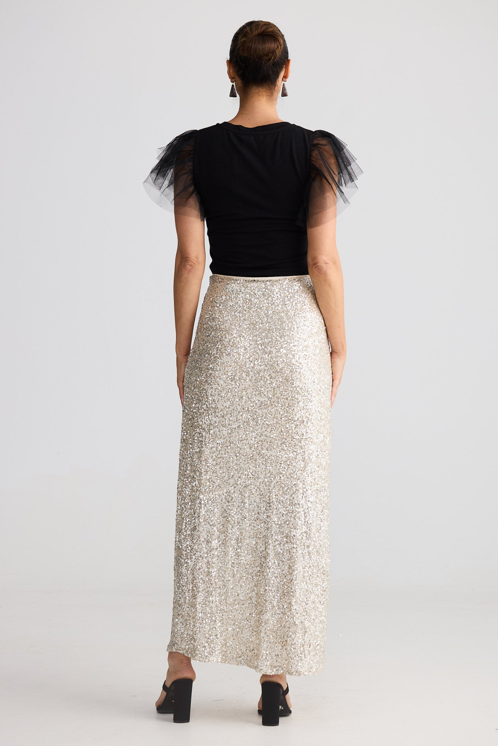 Woman wearing a black top with tulle sleeves and a silver sequin skirt on a white background