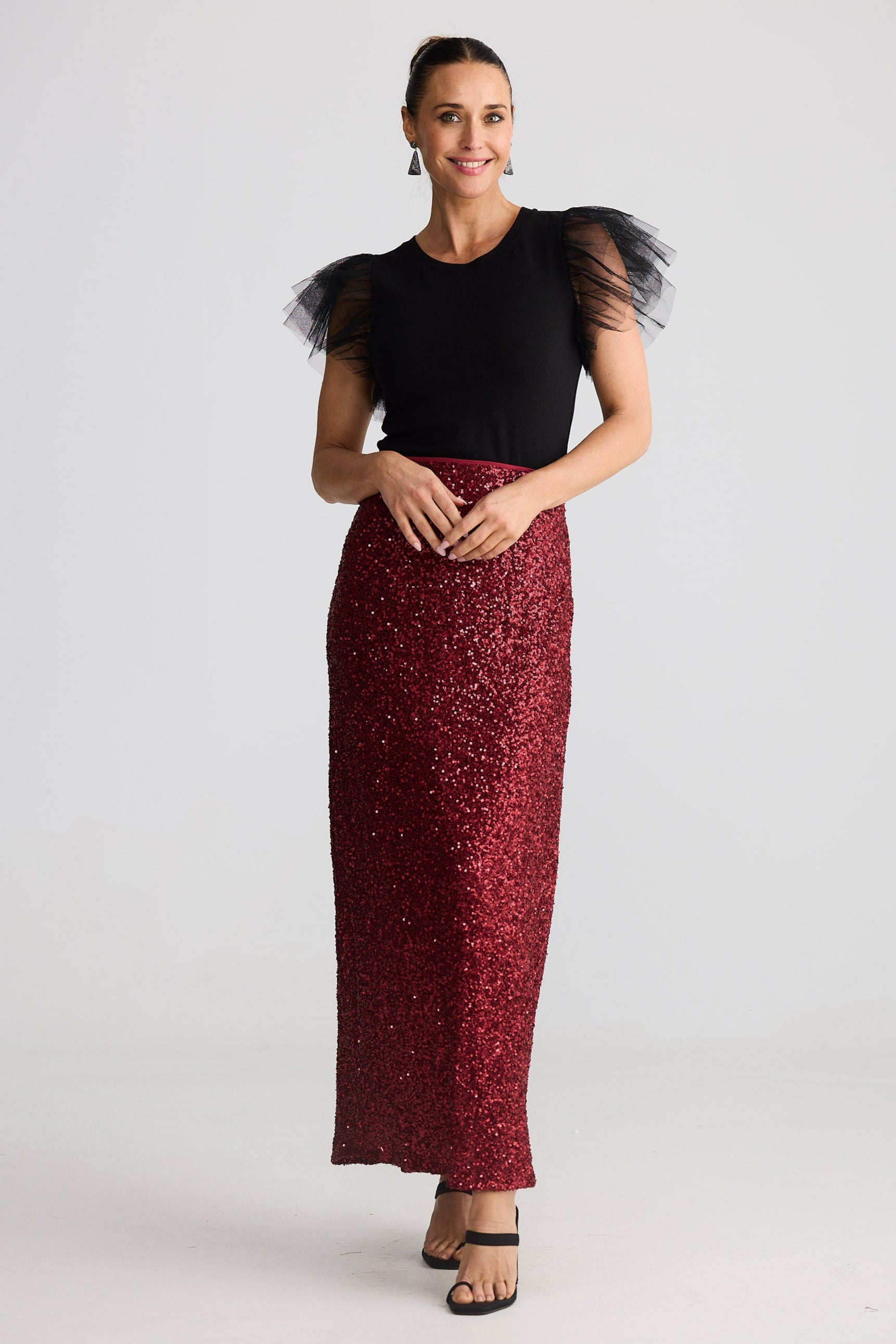 Woman wearing a black top with sheer sleeves and a red sequin skirt on a white background