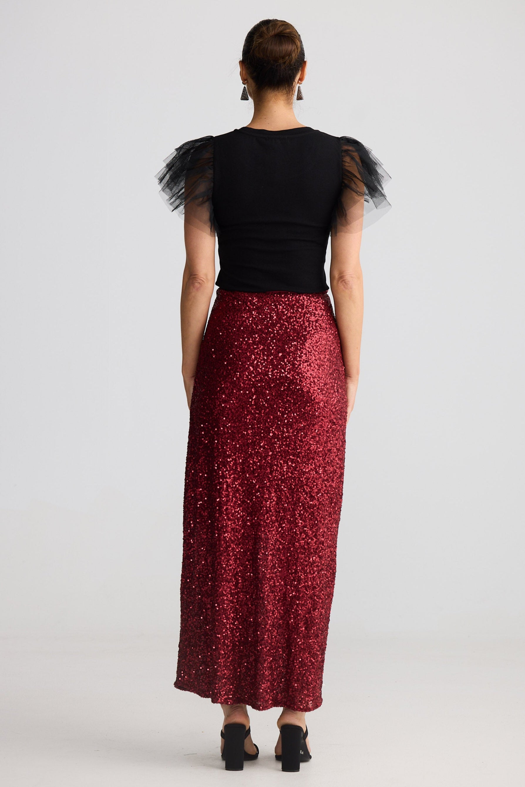 Person wearing a black top with sheer sleeves and a red sequined skirt on a white background