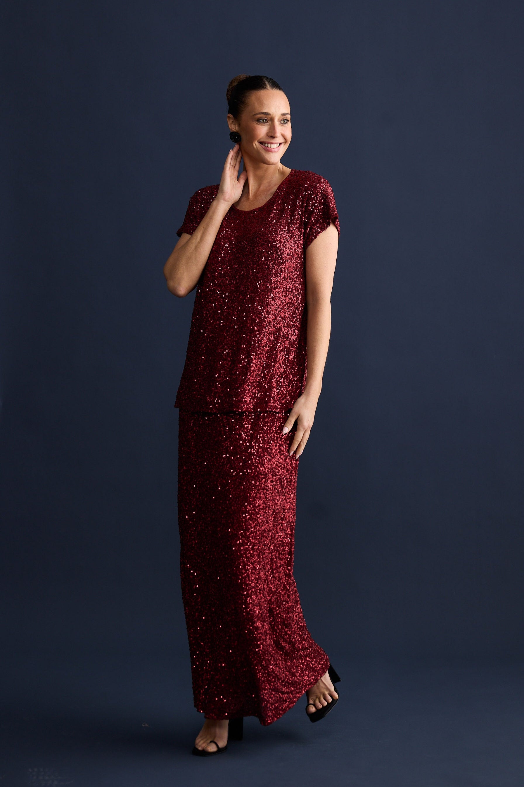 Woman wearing a long burgundy sequin skirt and t-shirt against a dark background