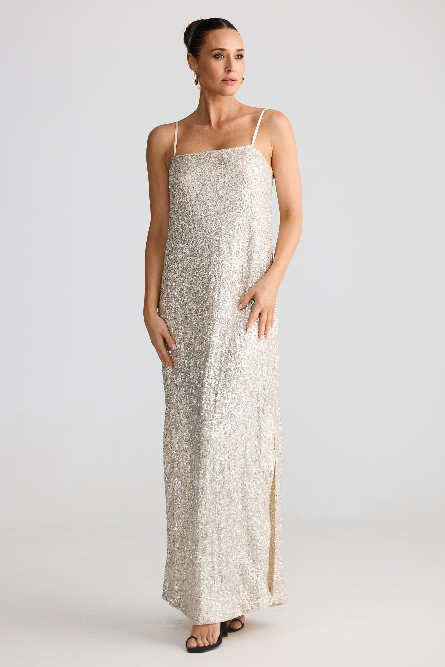 Woman wearing a long, light-colored sequin dress with thin straps on a white background