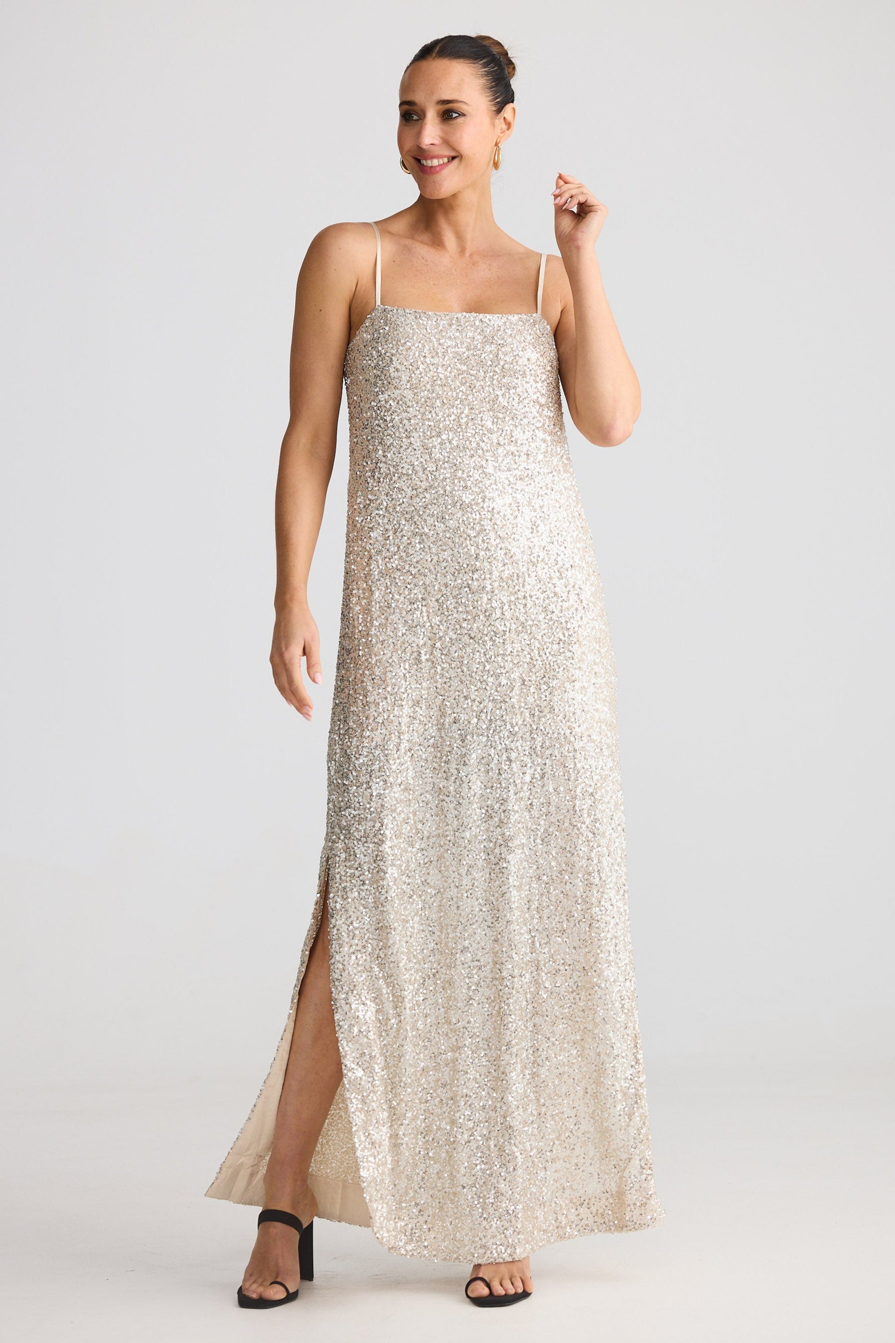 Woman wearing a long, light-colored sequin dress with thin straps on a white background