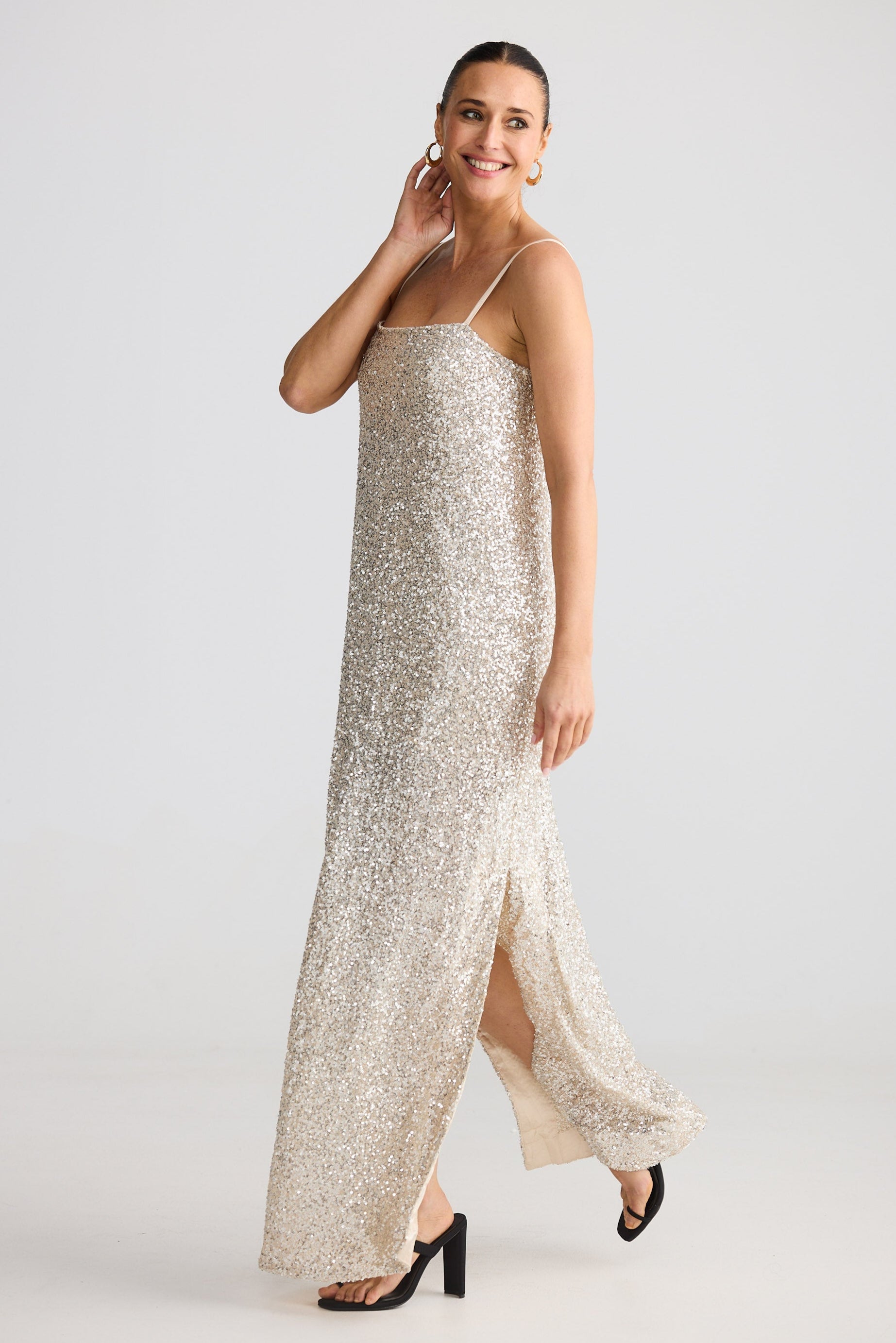 Woman wearing a long, light-colored sequin dress with thin straps on a white background