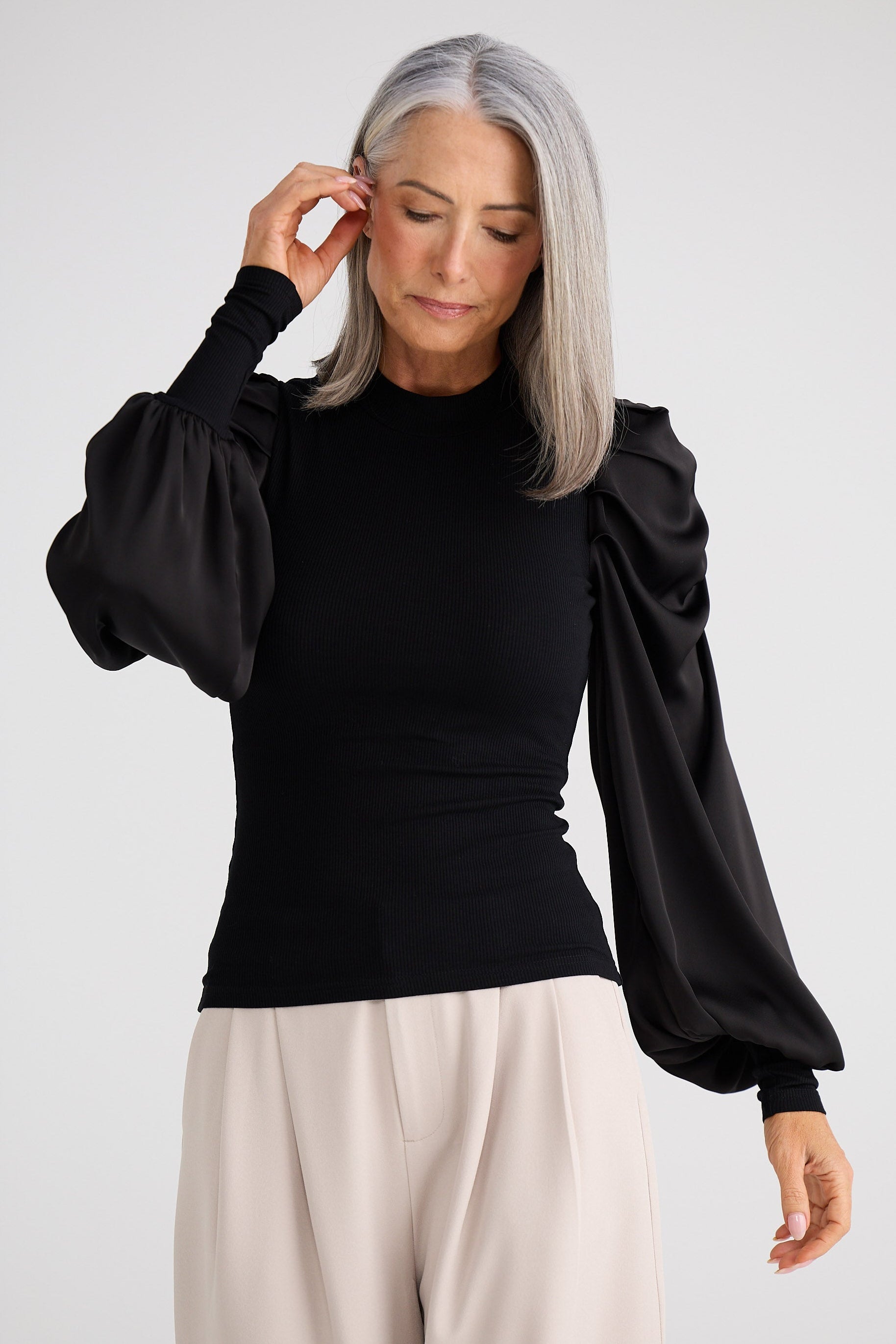 Woman wearing a black blouse with puffed sleeves and beige pants on a white background