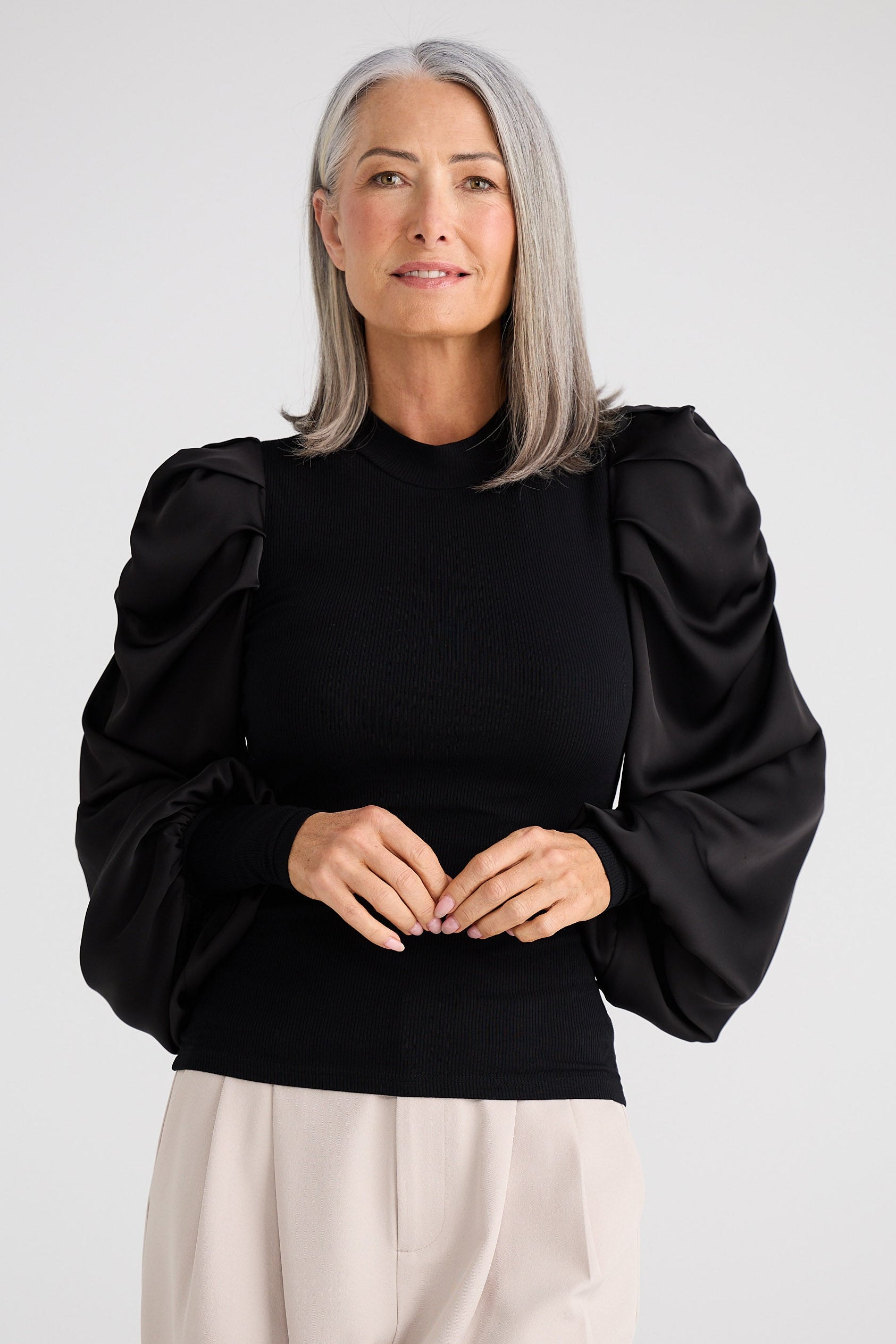 Woman wearing a black top with puffed sleeves and beige pants on a white background