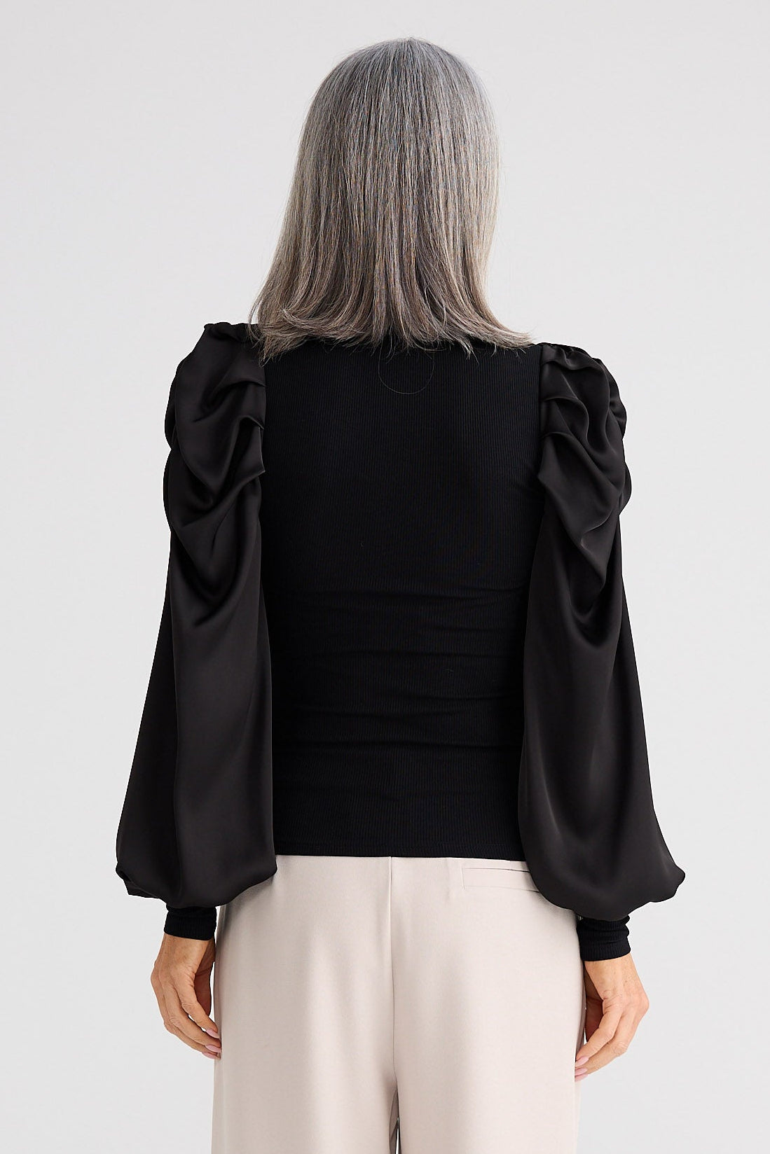 Person wearing a black blouse with ruffled sleeves and beige pants on a white background