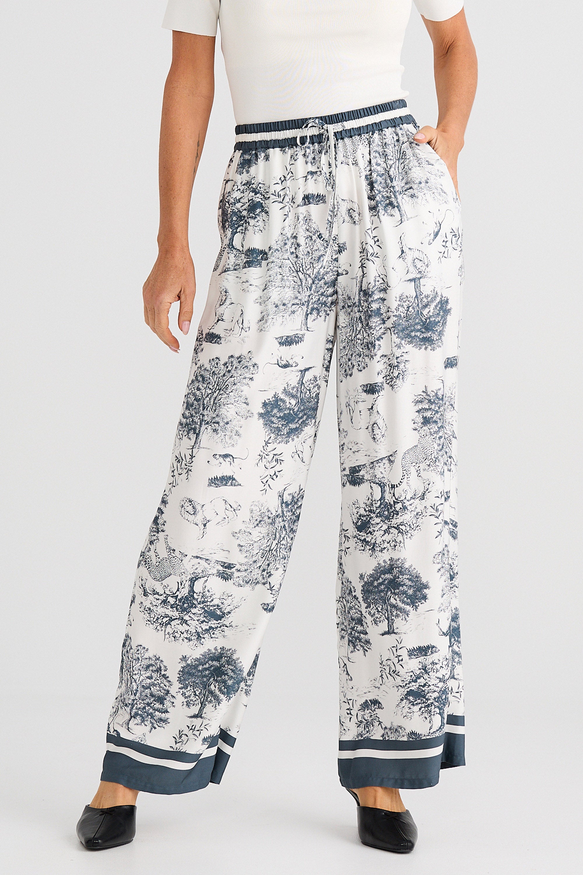Person wearing white floral-patterned pants with a white background