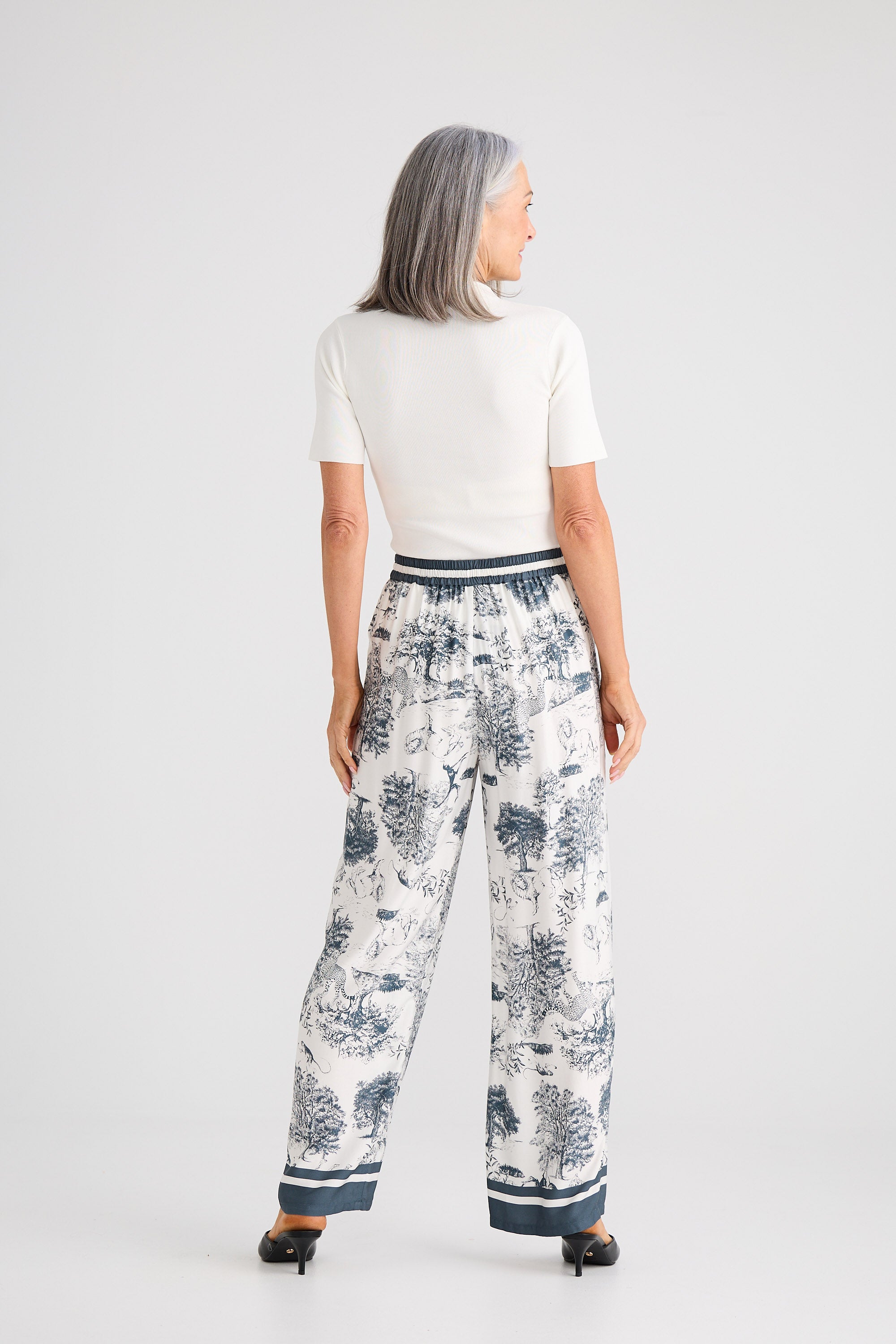 Woman wearing a white top and patterned pants on a plain background
