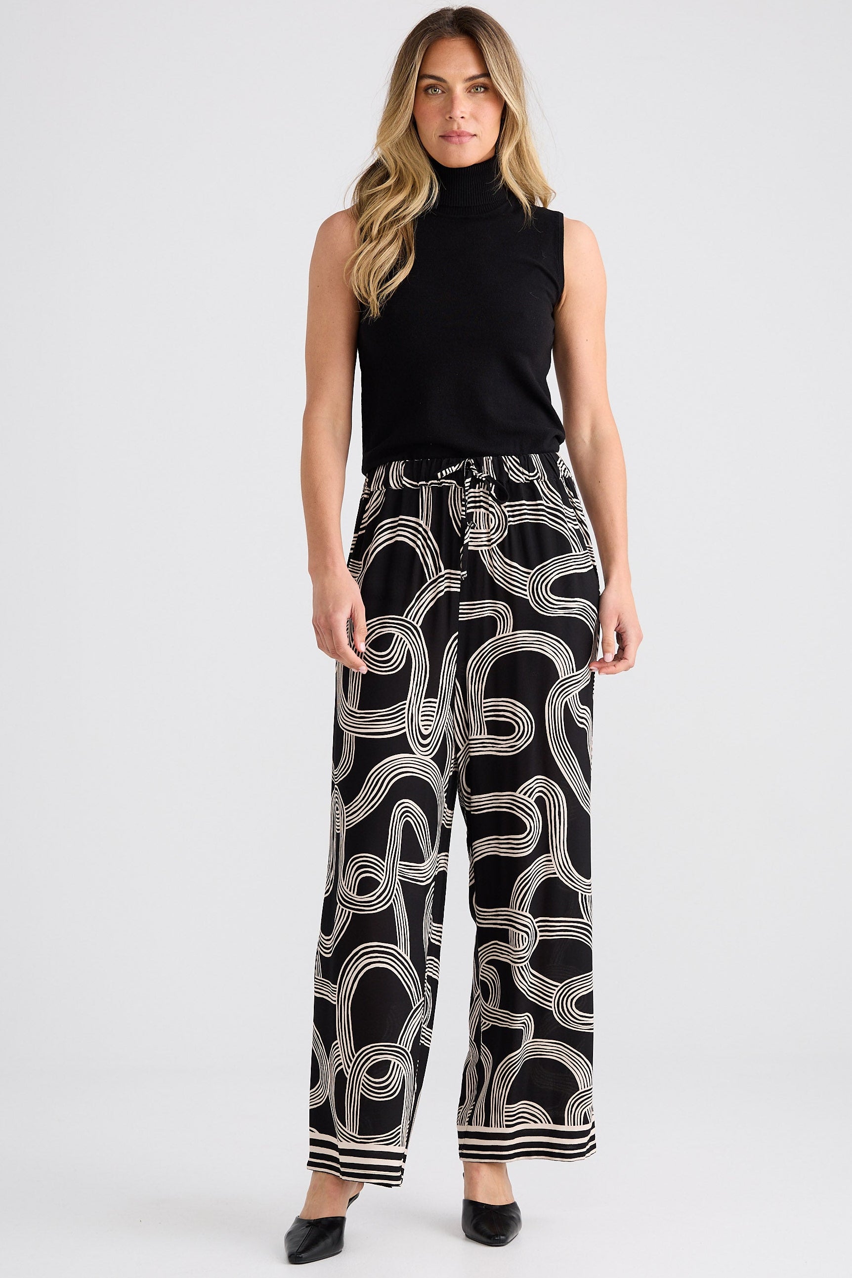 Woman wearing a black sleeveless top and patterned pants on a white background