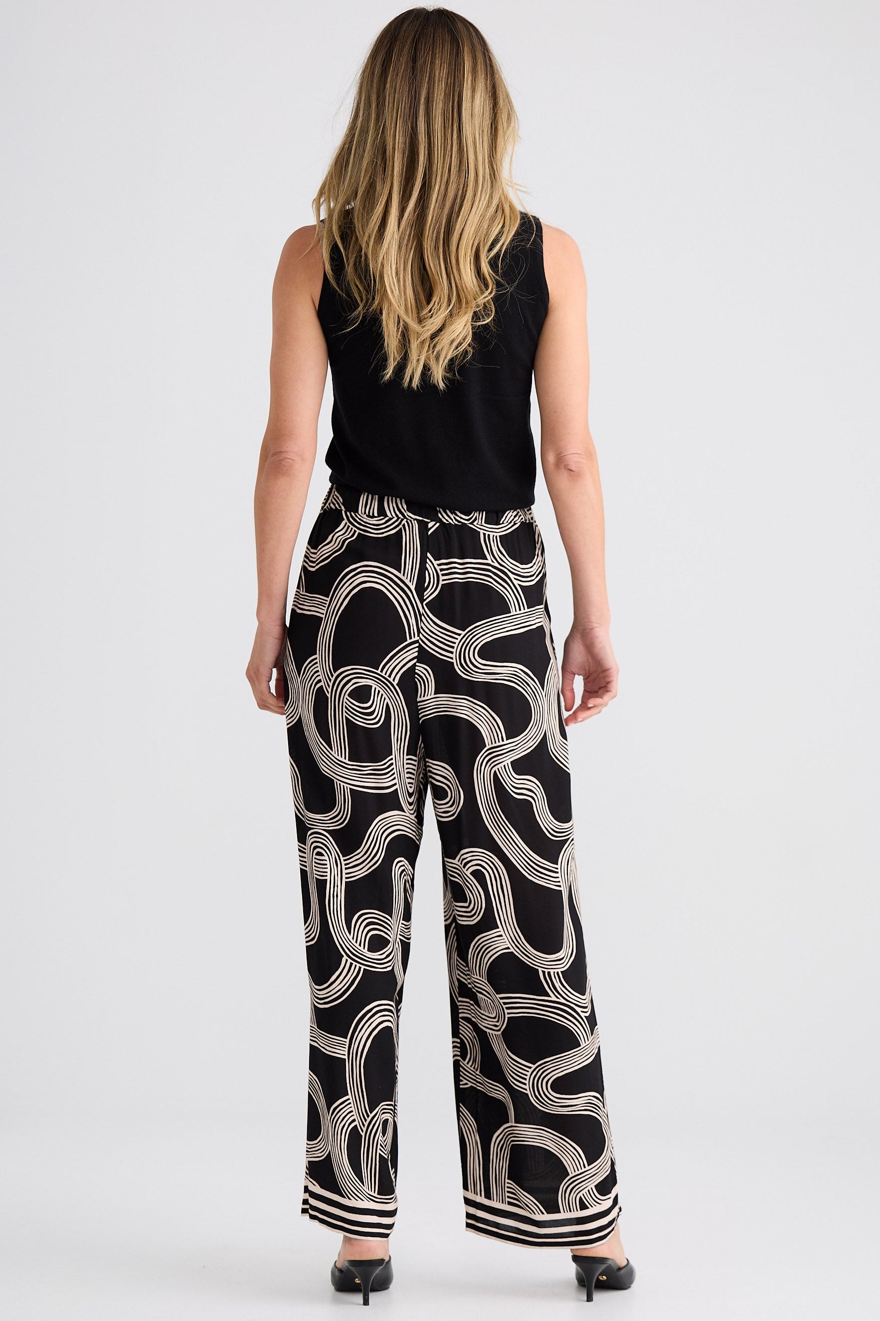 Woman wearing a black sleeveless top and patterned pants on a white background