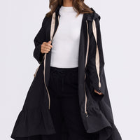 Model wearing Hyacinth Raincoat in black with hood and long sleeves, front view on white background