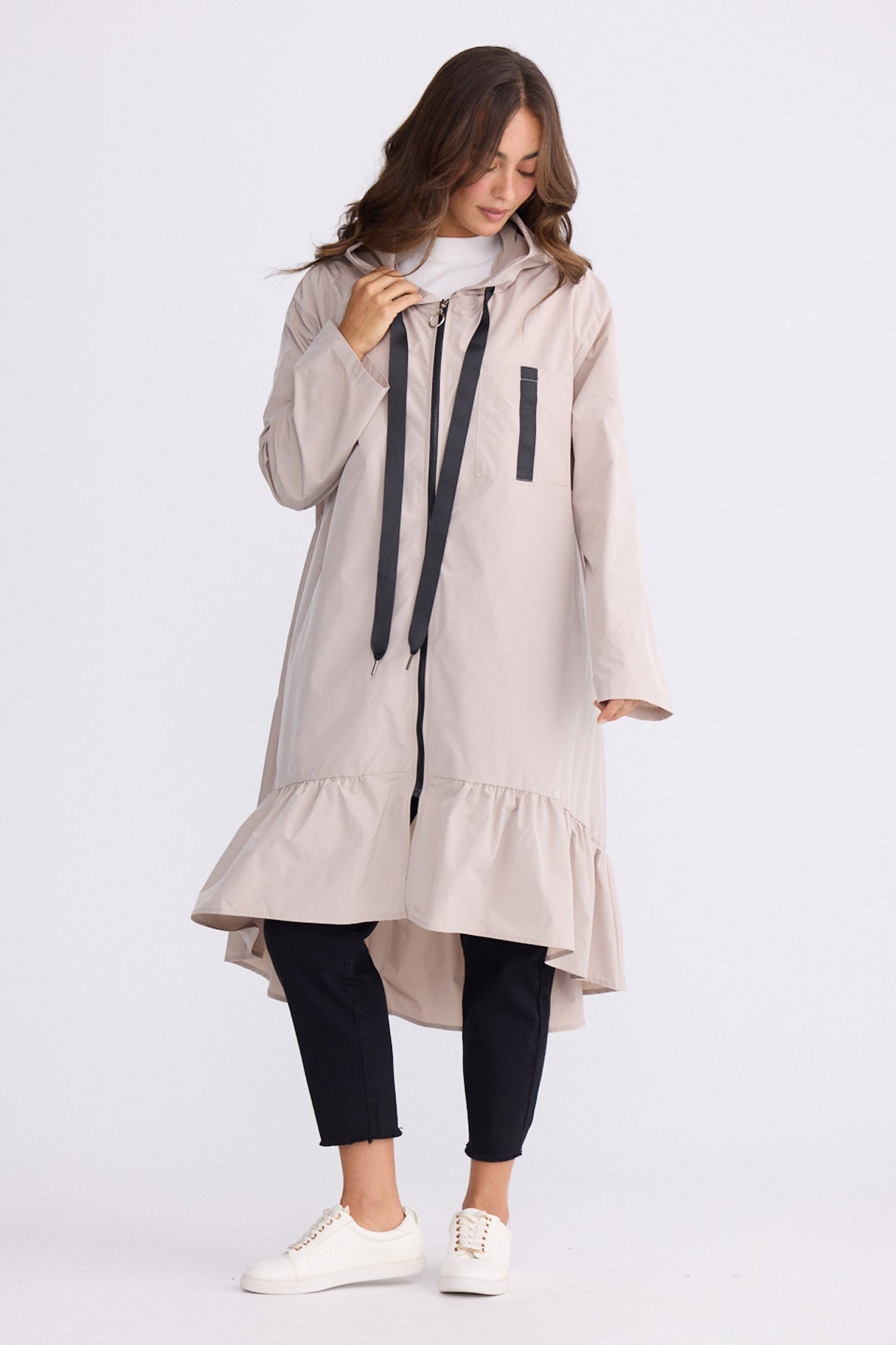 Woman wearing a long beige coat with ruffled details on white background