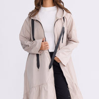Model wearing Hyacinth Raincoat in beige with hood and long sleeves, front view on white background