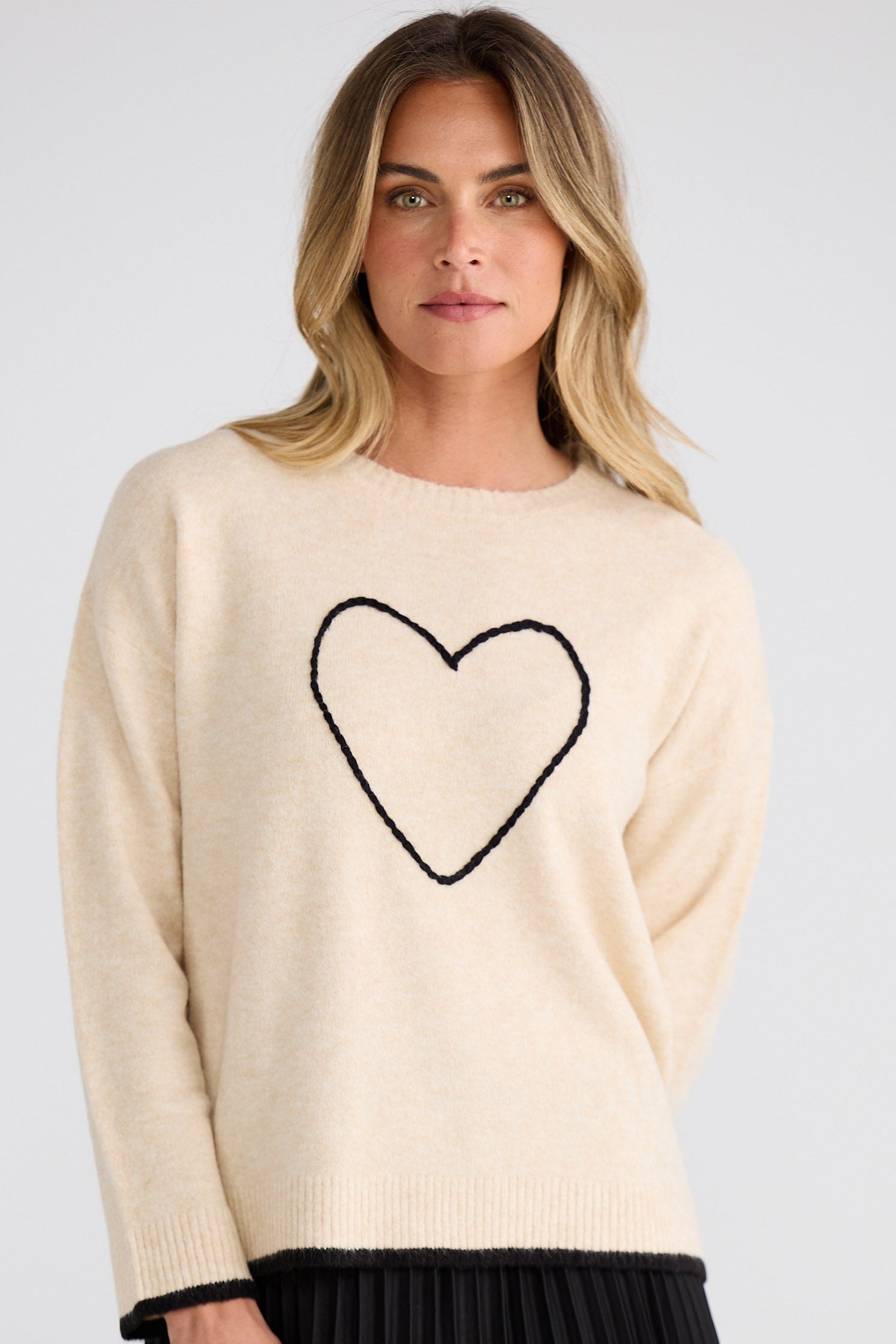 Woman wearing a cream sweater with a black heart design on a plain background
