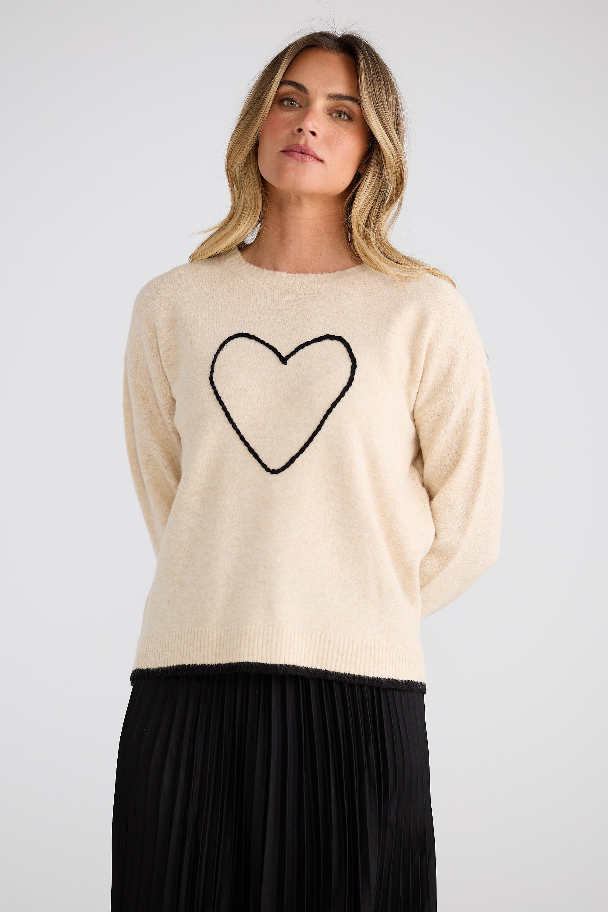 Woman wearing a beige sweater with a black heart design on a plain background