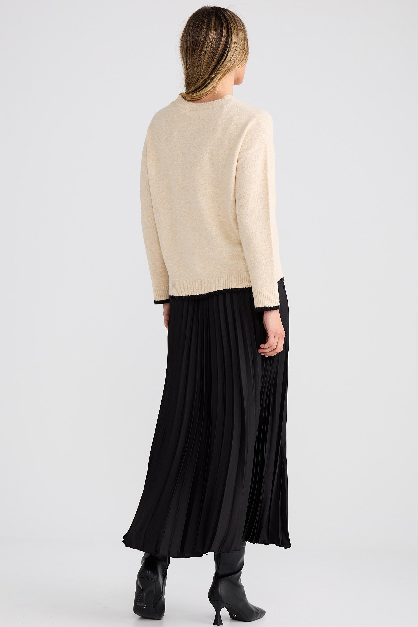 Person wearing a beige sweater and black pleated skirt on a white background
