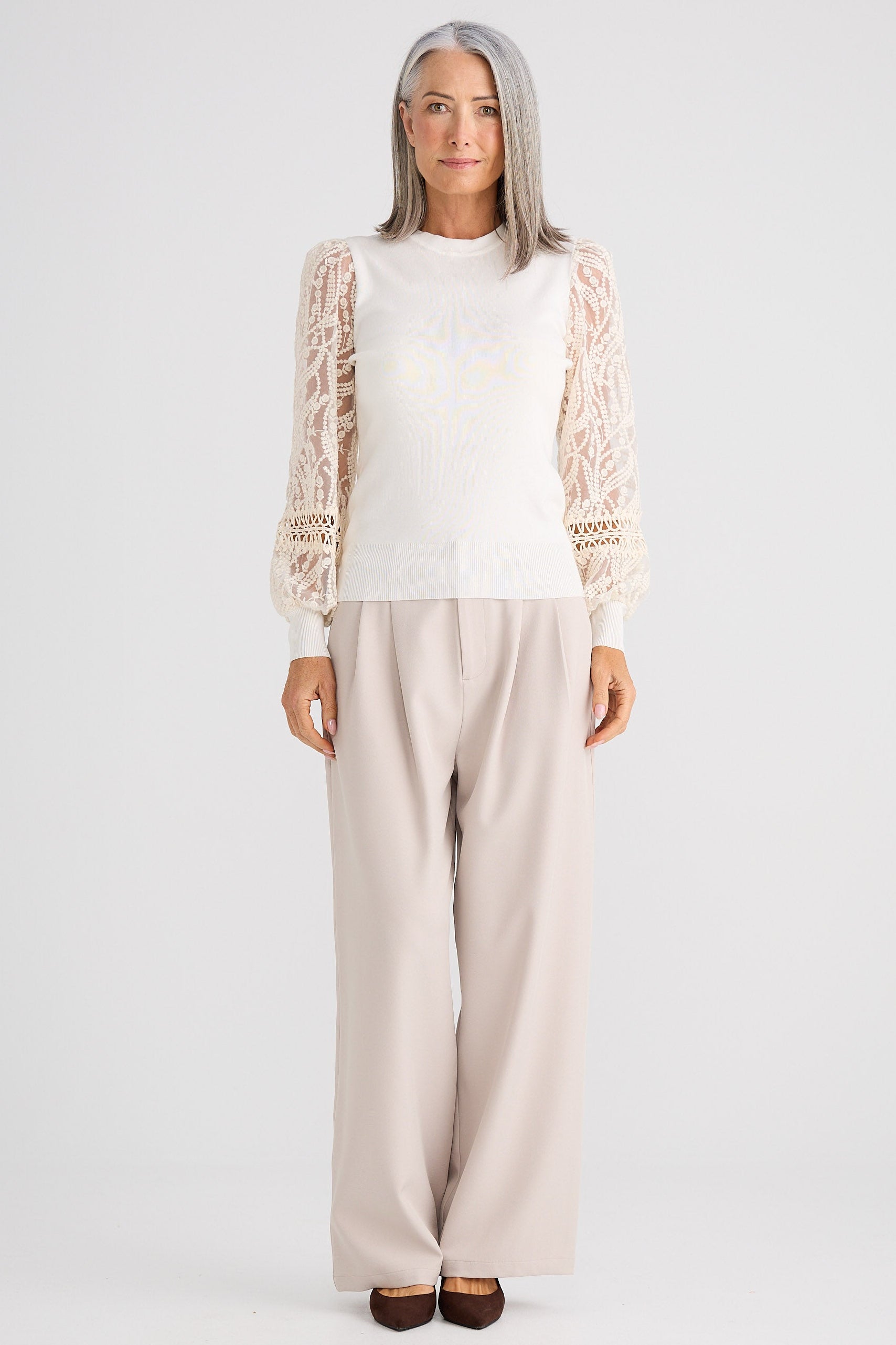 Person wearing a white top with lace sleeves and beige pants on a white background