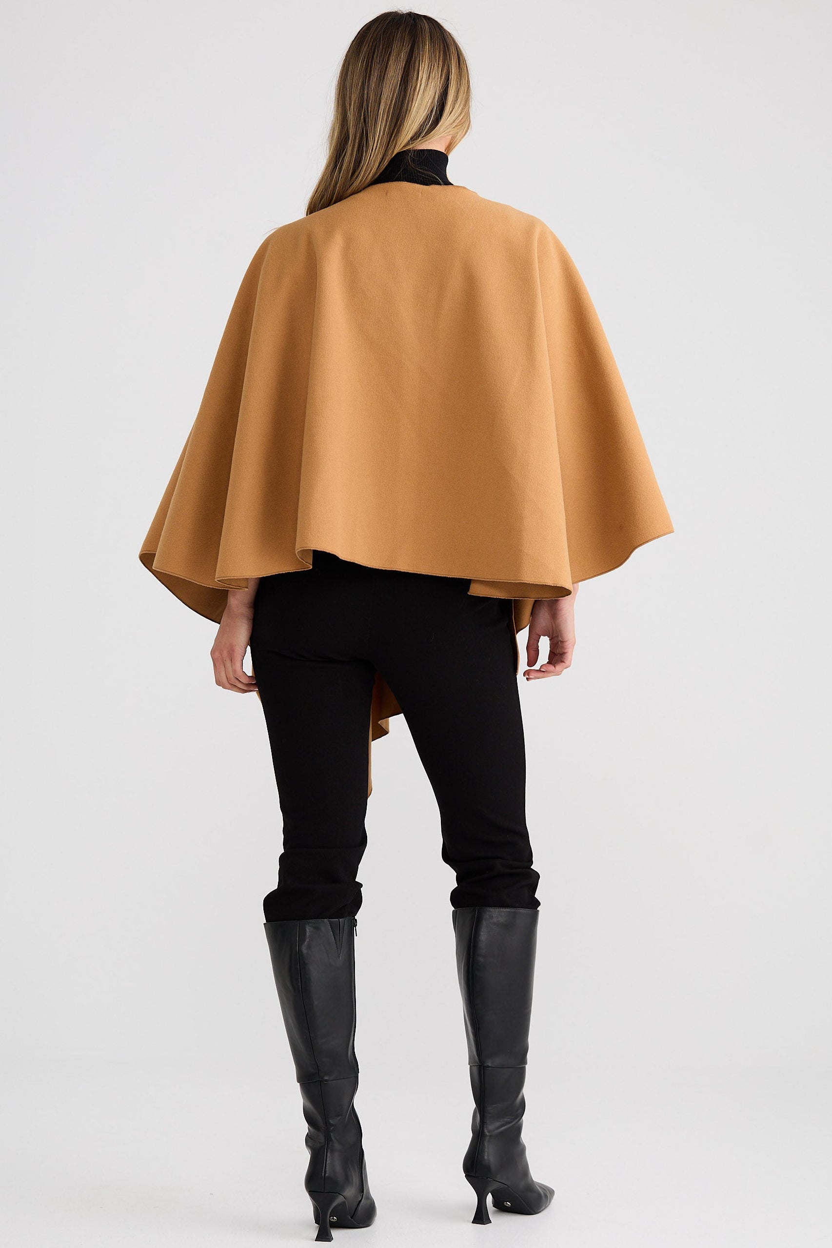 Woman wearing a mustard yellow cape over a black outfit on a white background