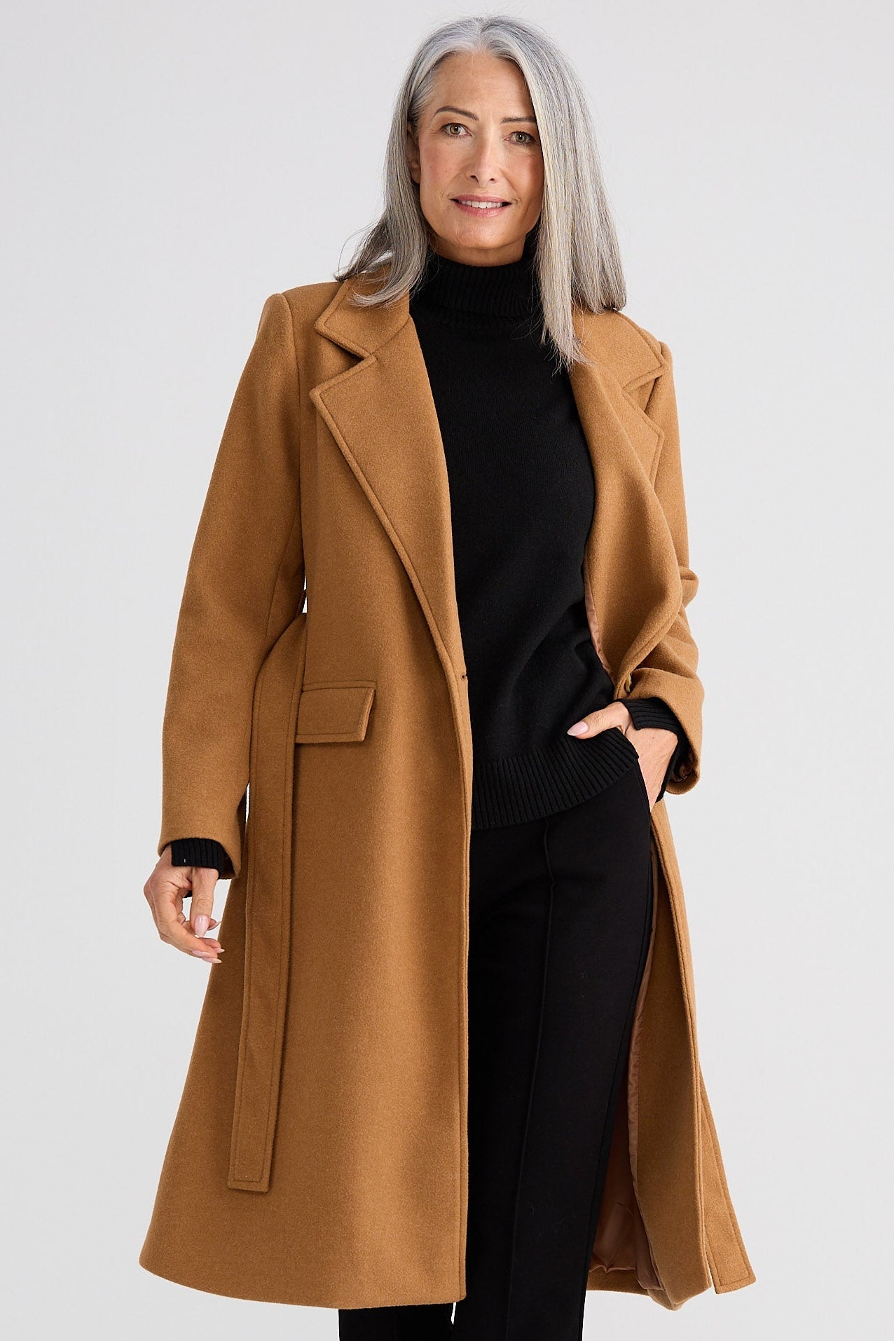 Woman wearing a tan coat over a black outfit on a white background