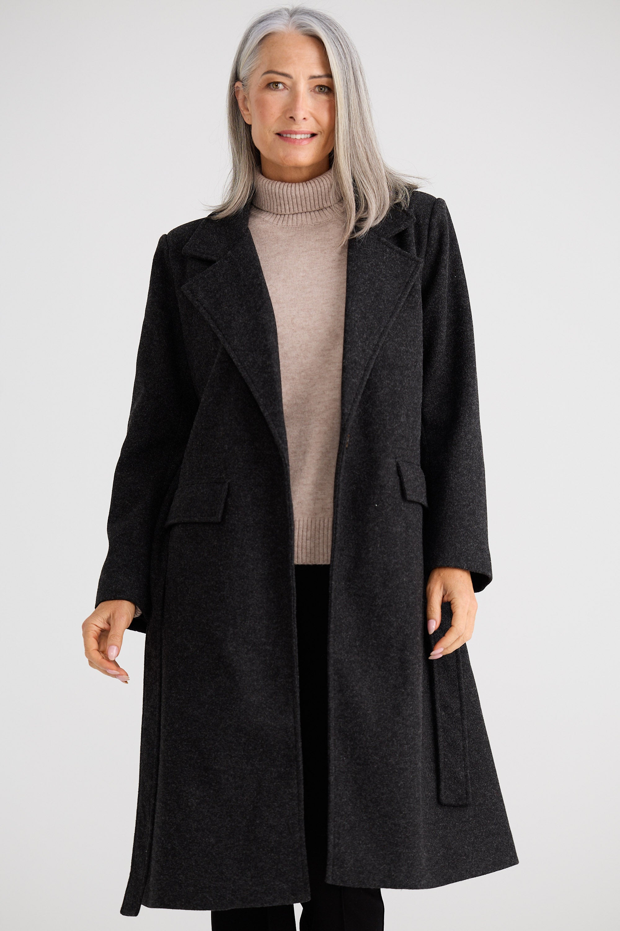 Woman wearing a black coat over a beige sweater on a white background