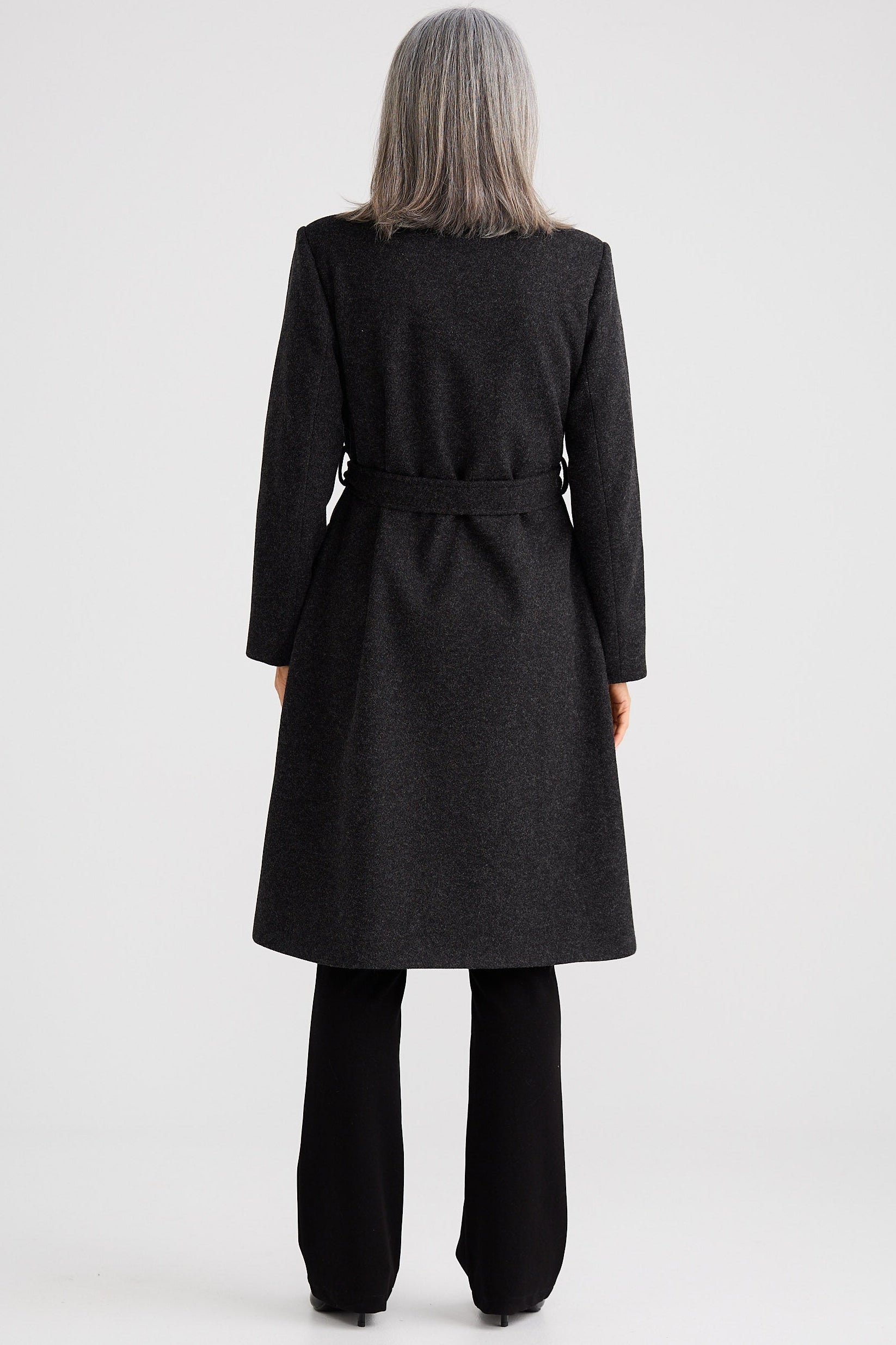 Person wearing a black coat standing against a white background