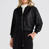 Woman wearing a black sequin jacket and black pants on a white background