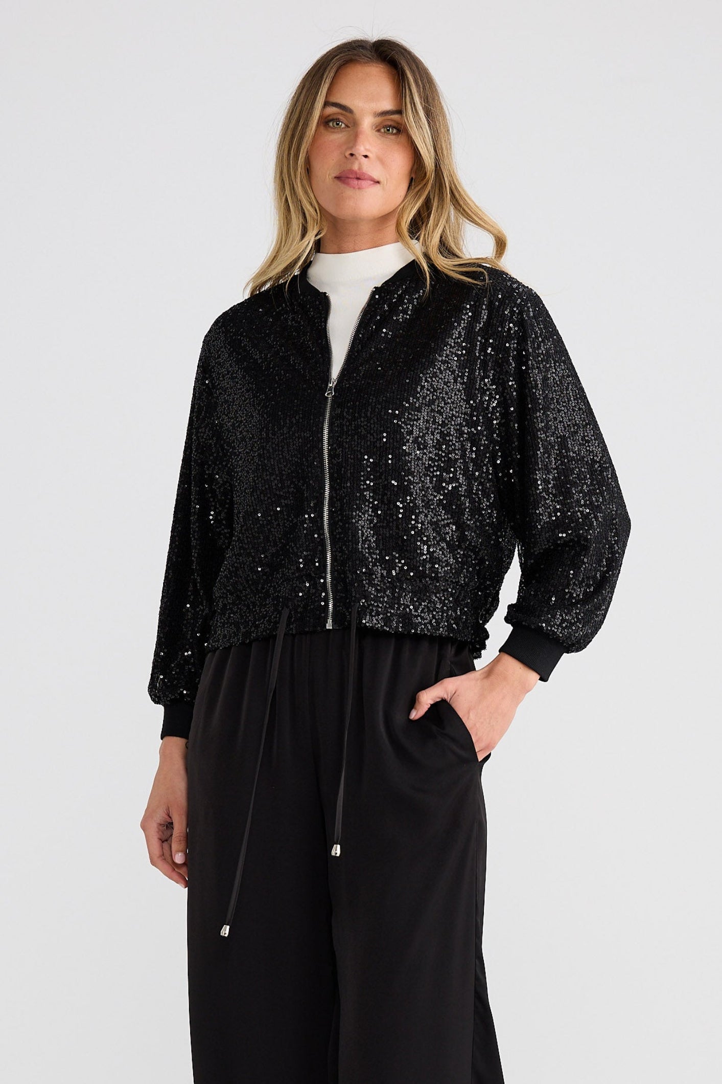 Woman wearing a black sequin jacket and black pants on a white background