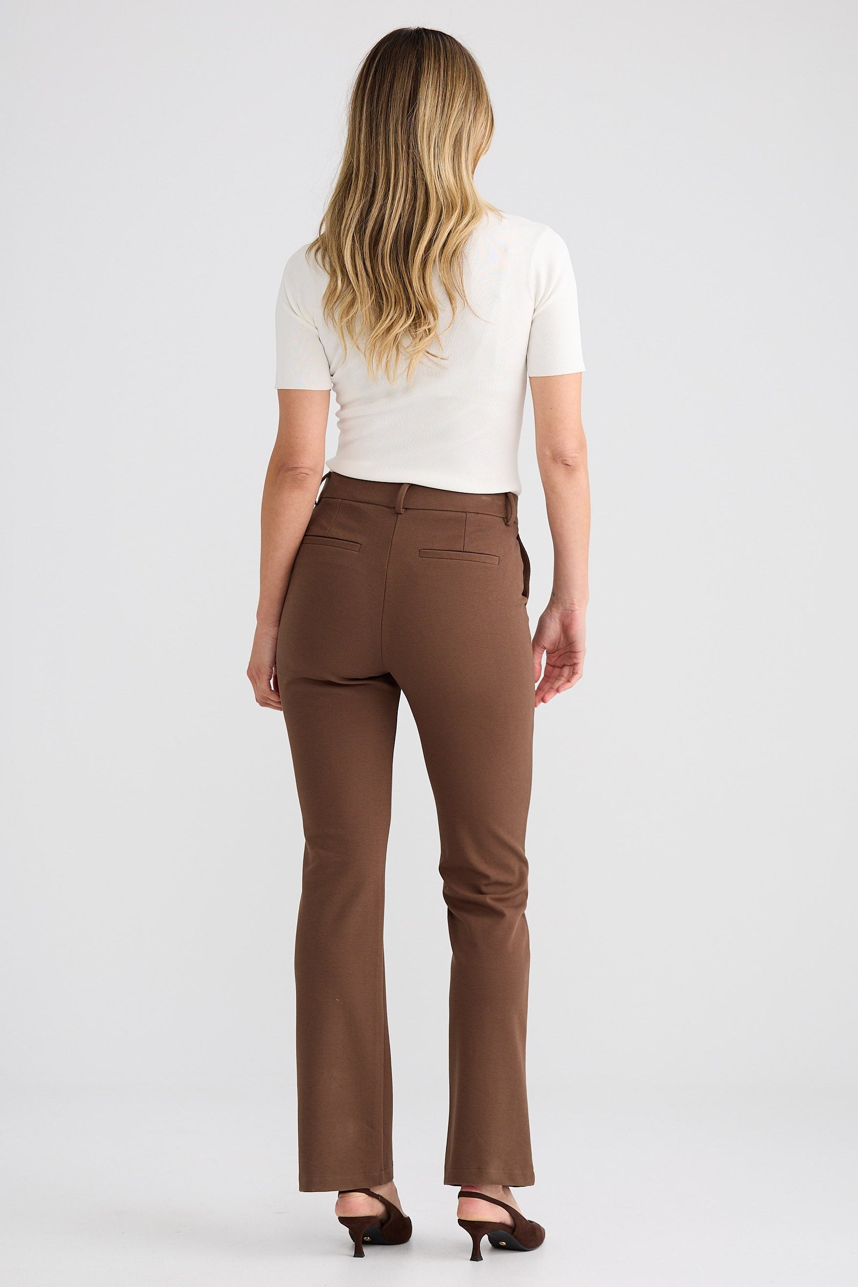 Woman wearing brown pants and a white top on a plain background