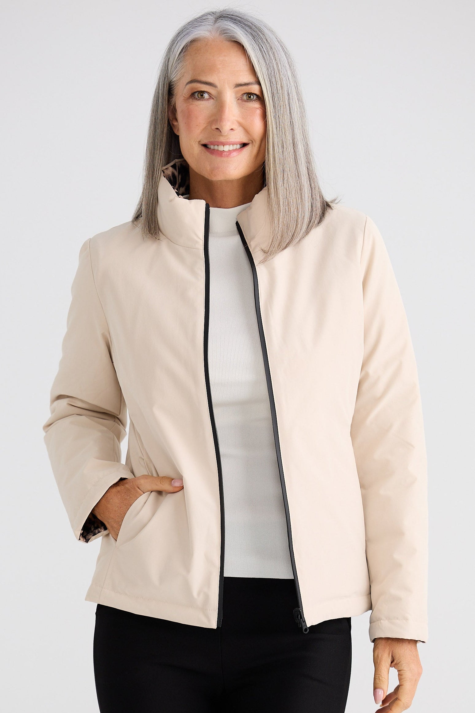 Woman wearing a beige jacket over a white shirt and black pants on a white background