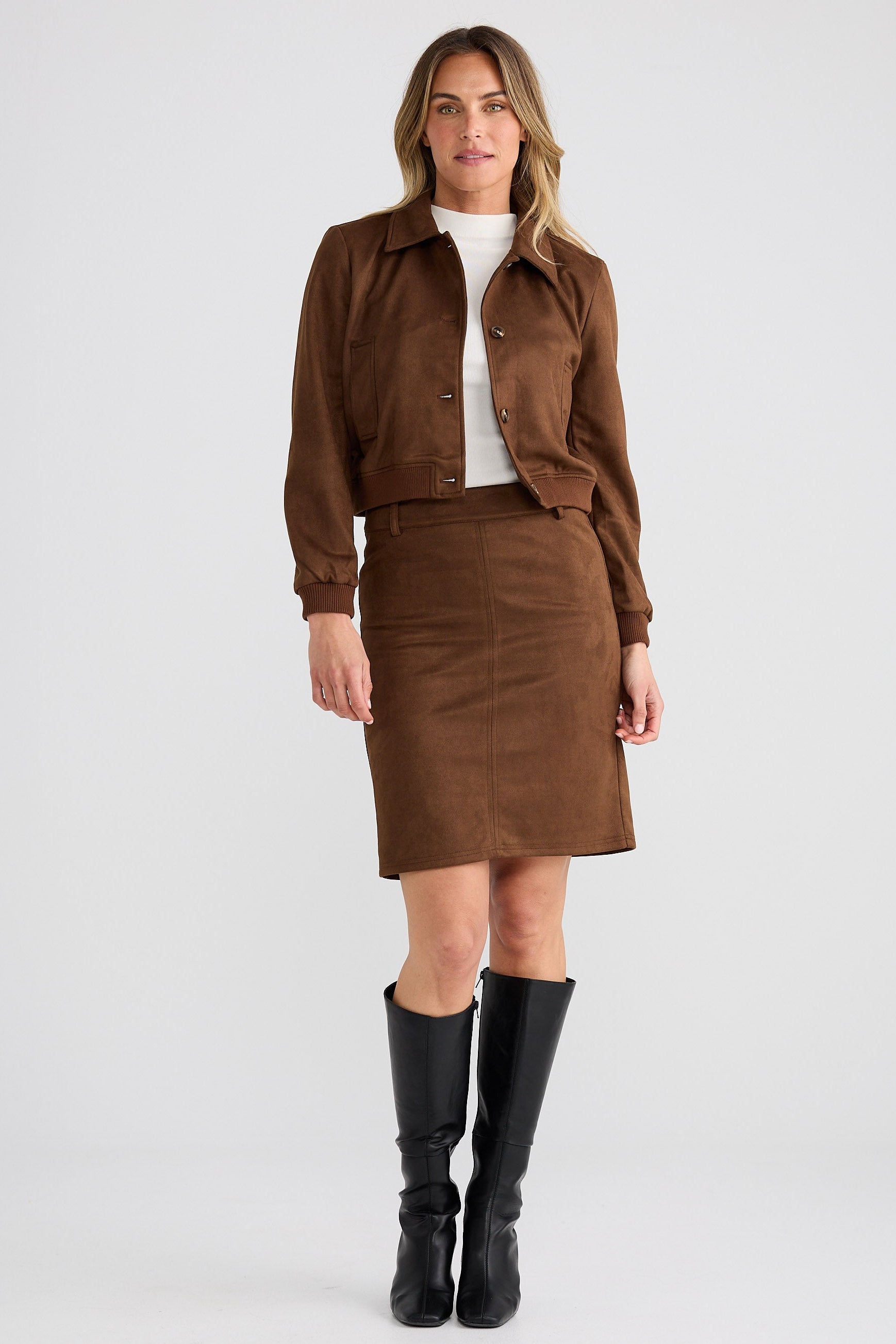 Woman wearing a brown jacket and skirt set with black knee-high boots on a white background
