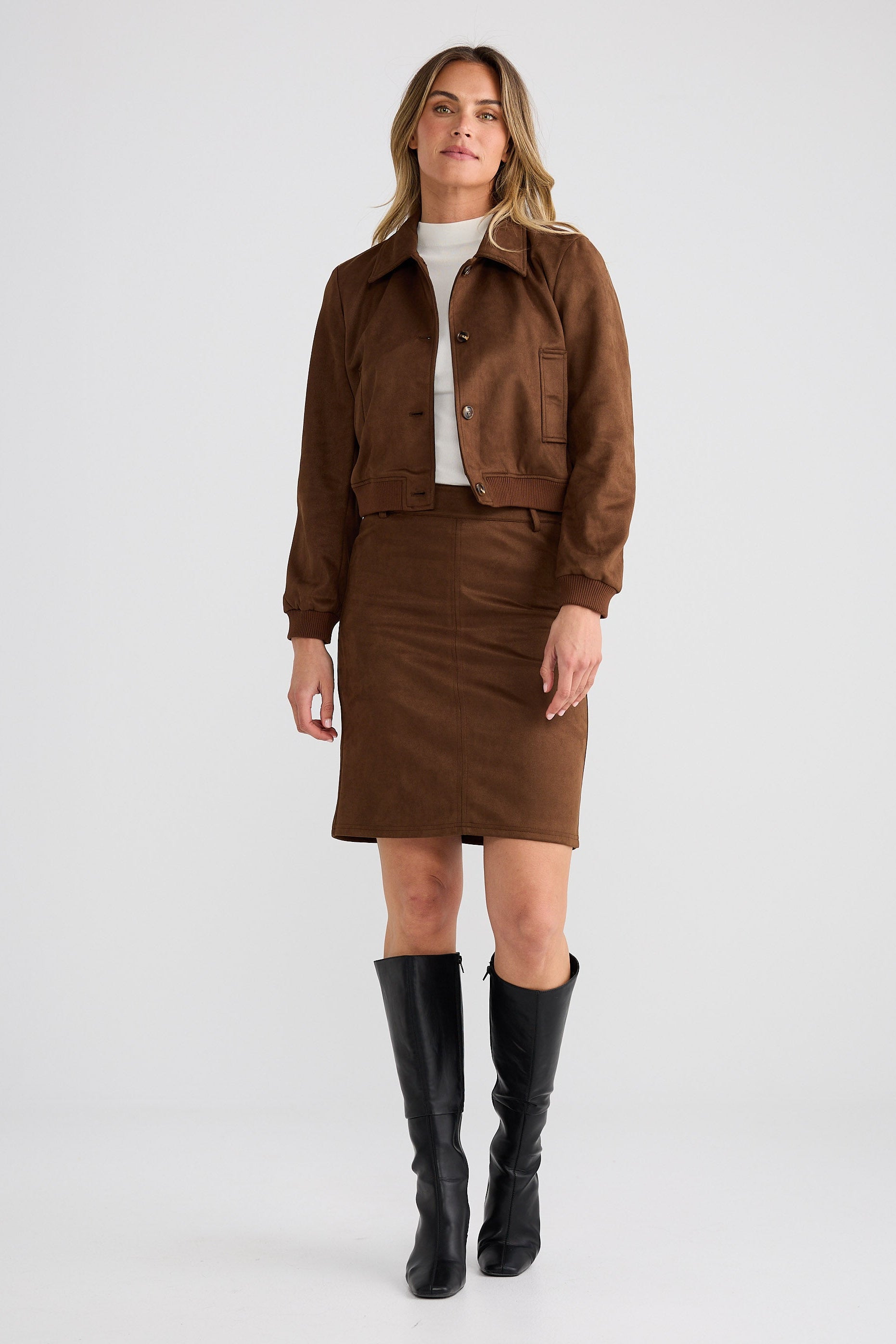Woman wearing a brown jacket and skirt with black boots on a white background