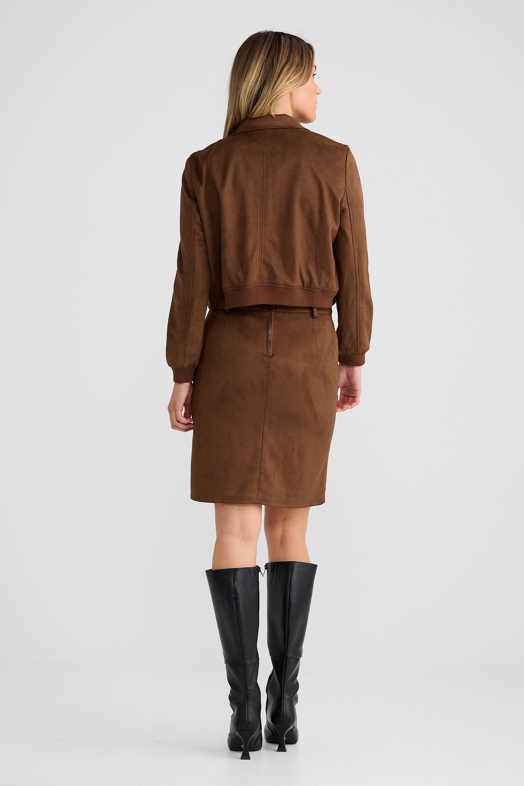 Person wearing a brown outfit with a jacket and skirt on a white background