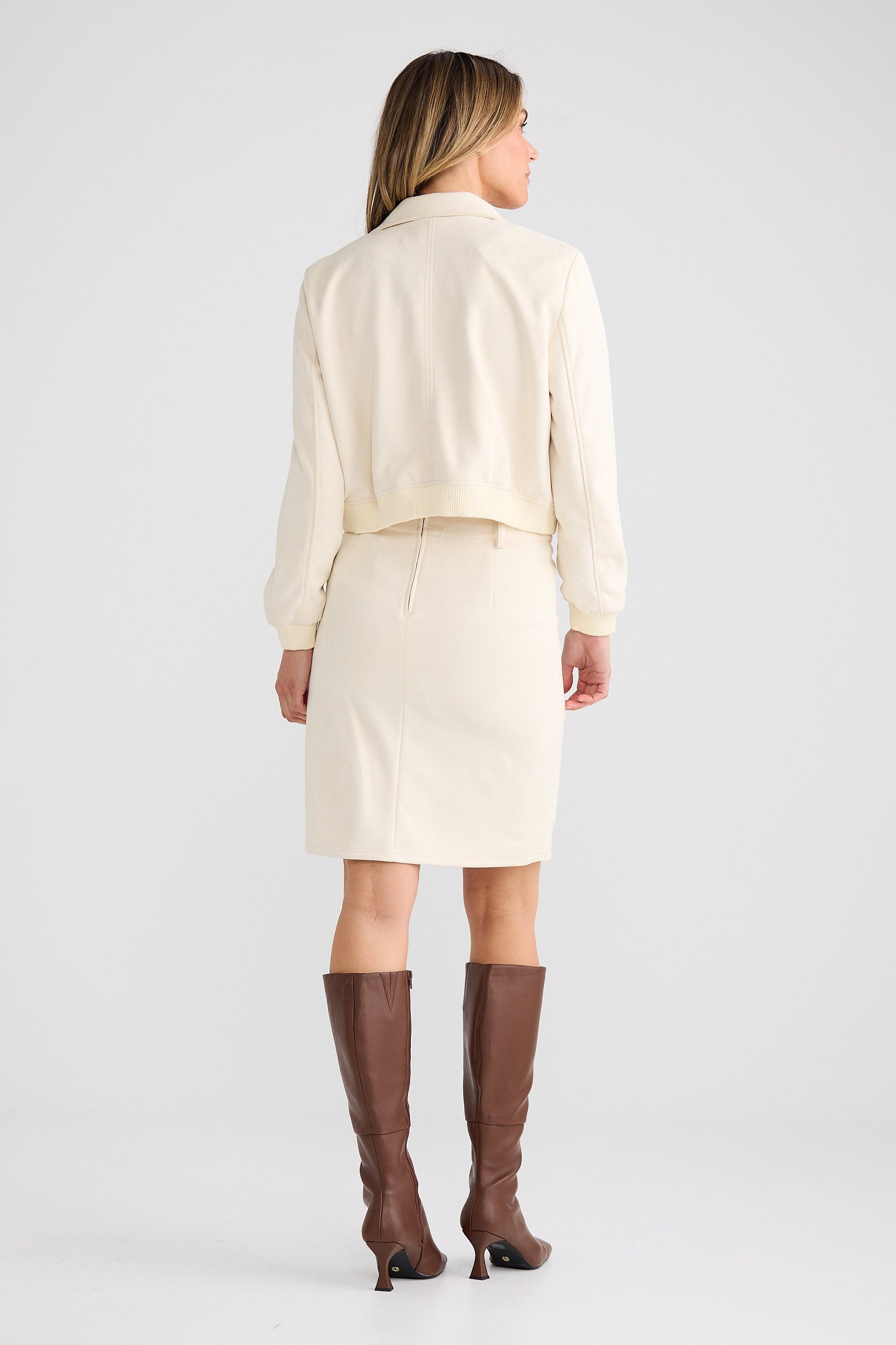 Woman wearing a cream-colored suit with brown knee-high boots on a white background