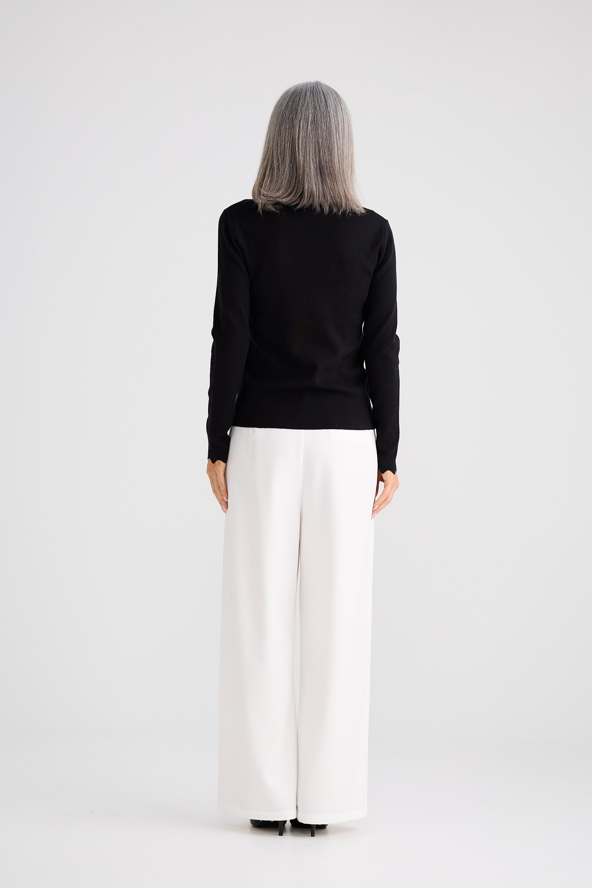 Person wearing a black sweater and white pants on a white background