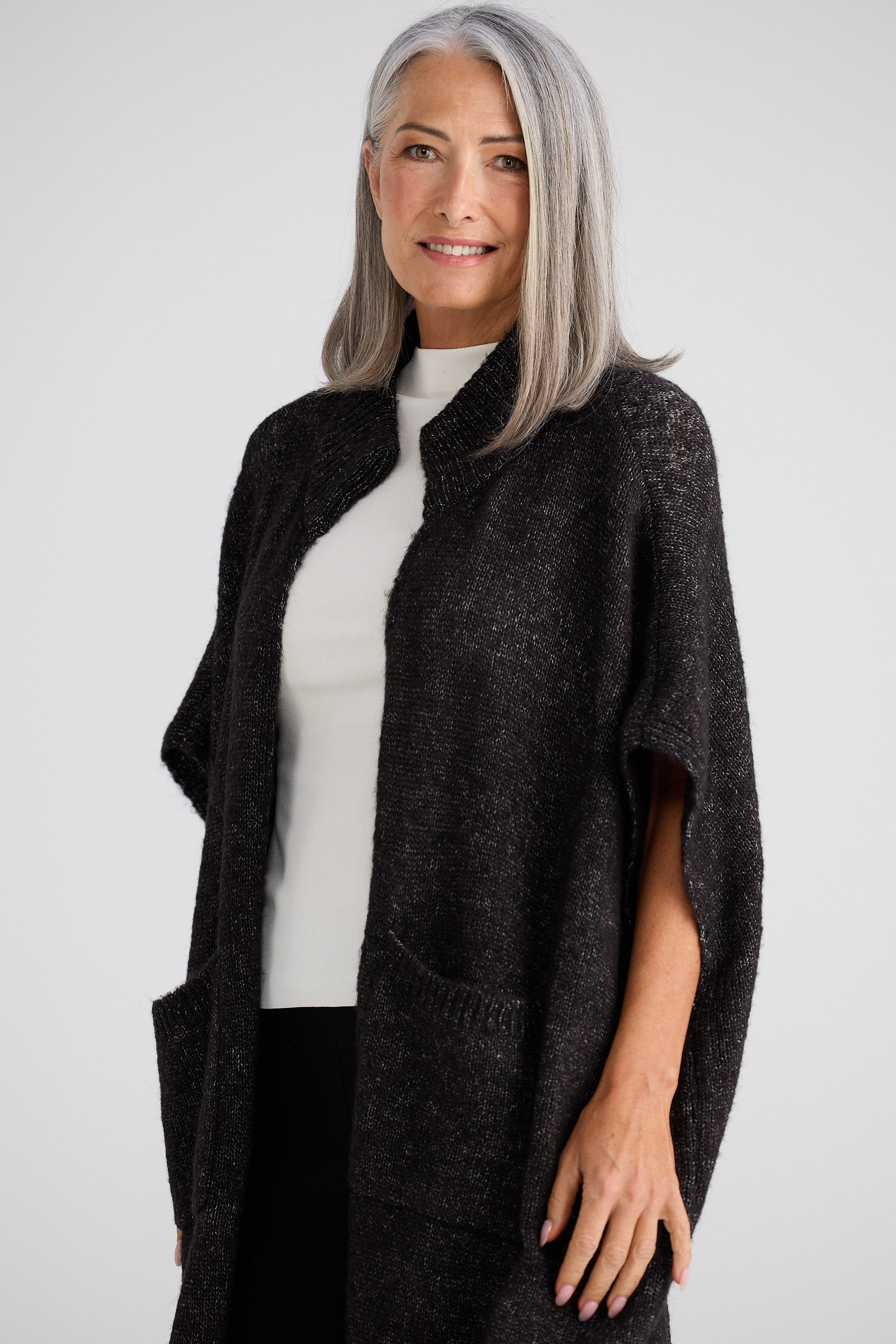 Woman wearing a dark gray poncho over a white top on a light gray background