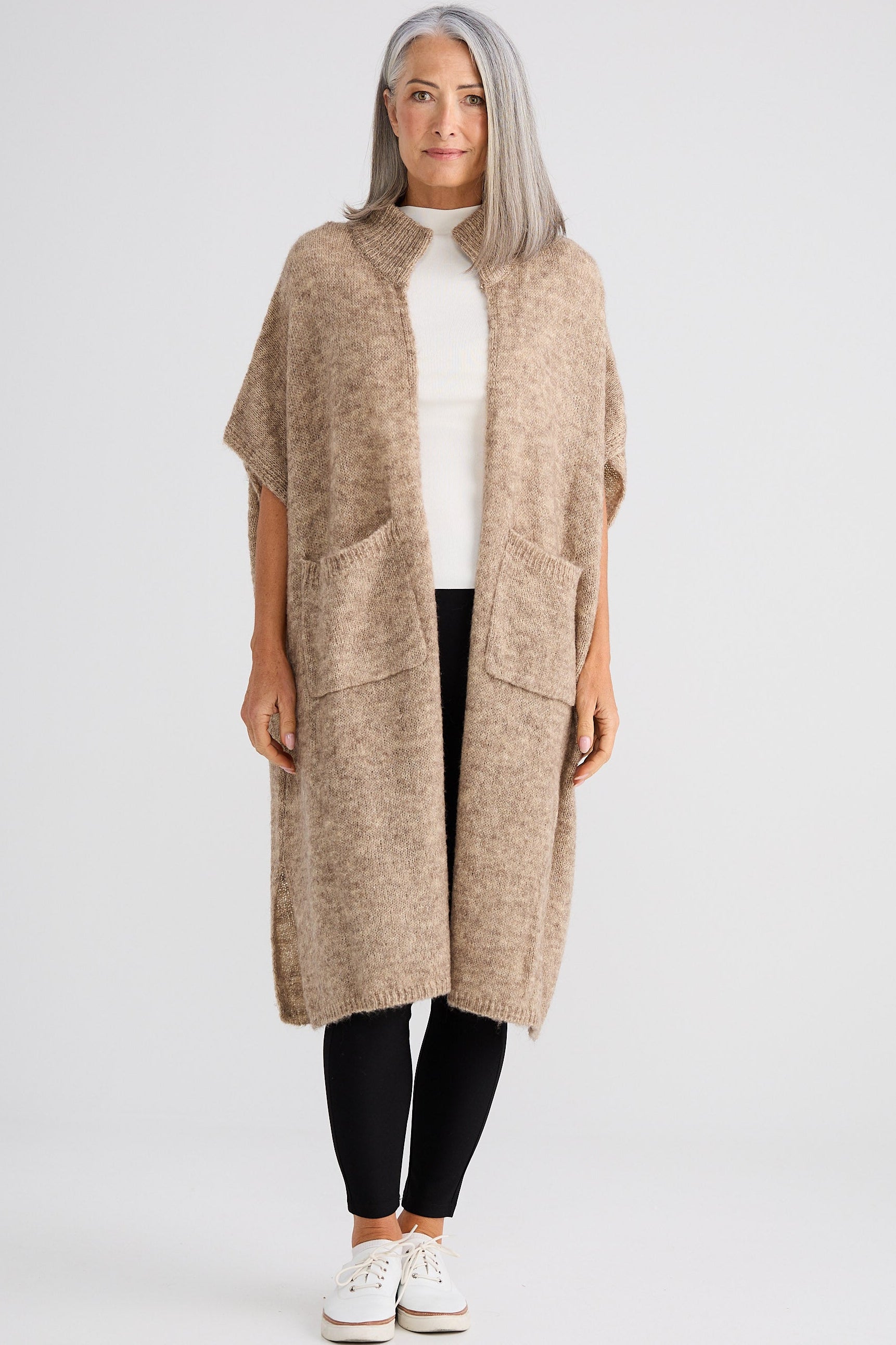 Woman wearing a long beige cardigan over a white top and black pants on a white background