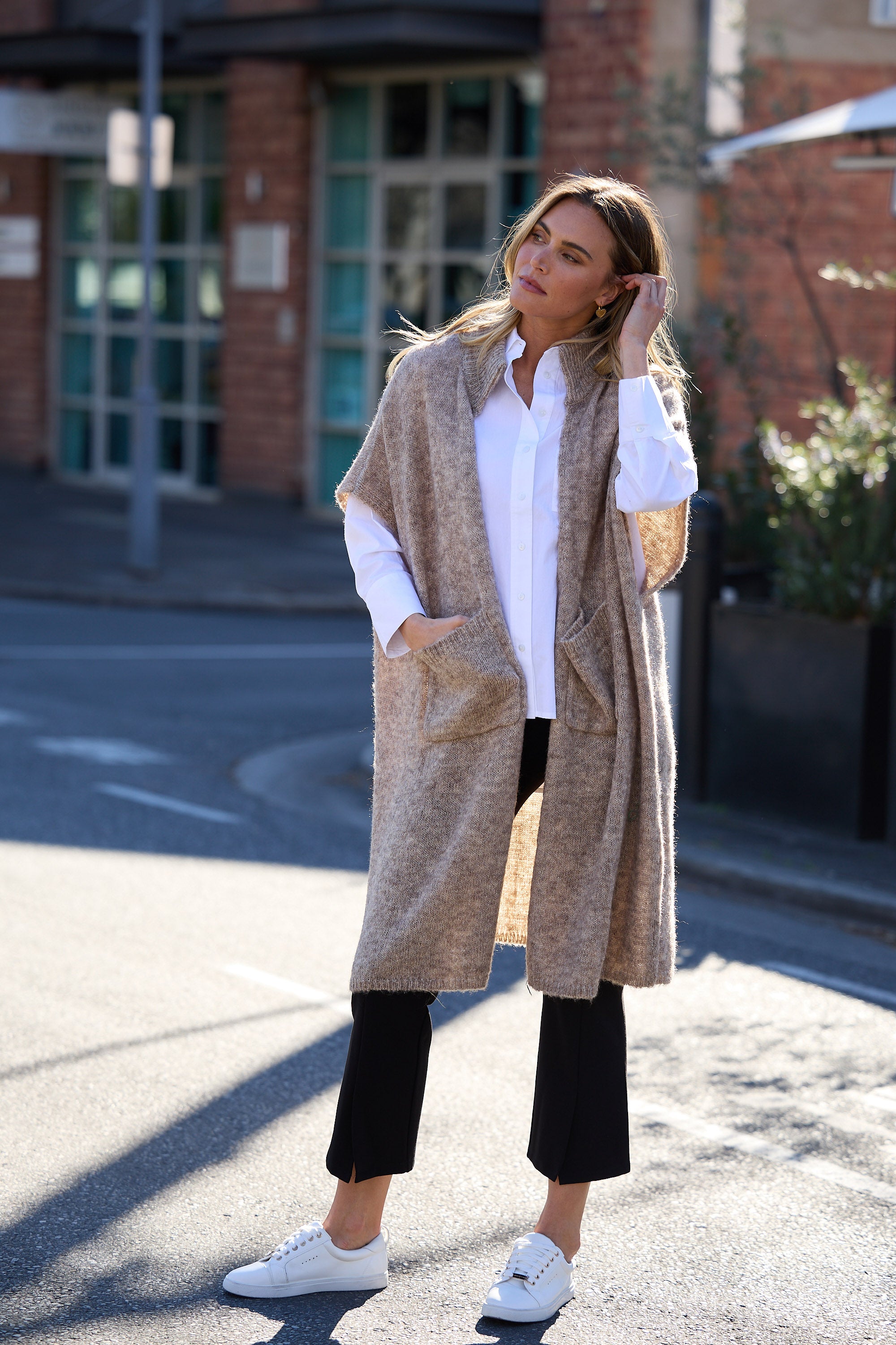 Woman wearing a beige poncho over a white shirt and black pants on a street.