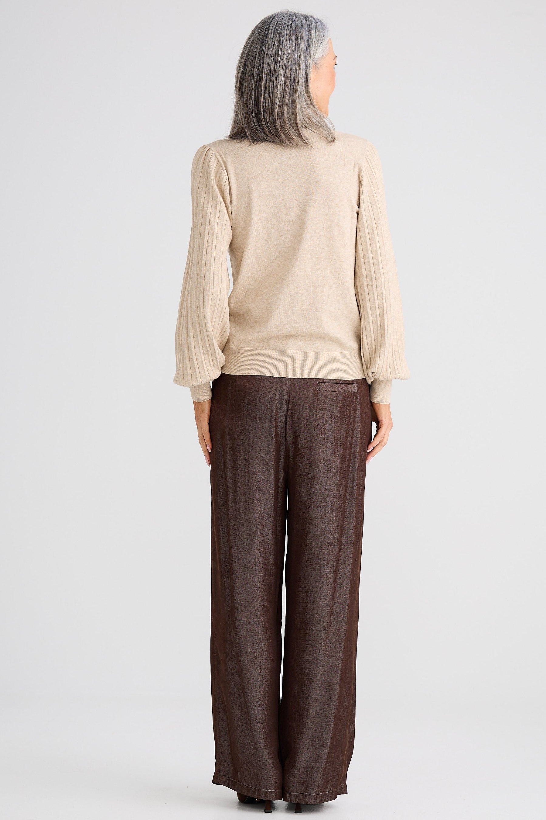 Person wearing a beige top and brown pants on a white background