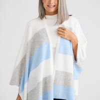 Woman wearing a striped poncho with gray, white, and blue colors on a plain background