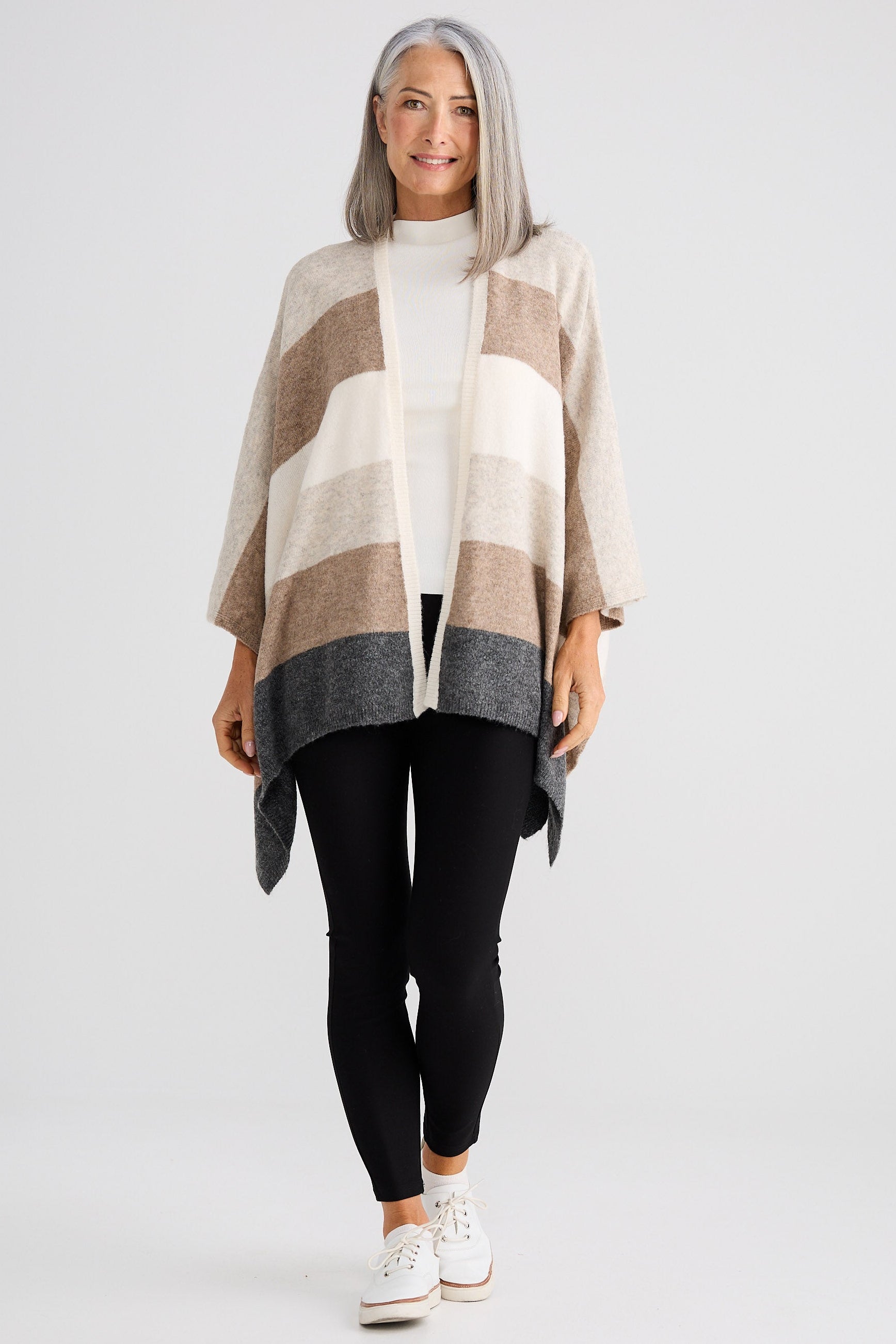 Woman wearing a striped poncho over a white sweater and black leggings on a white background