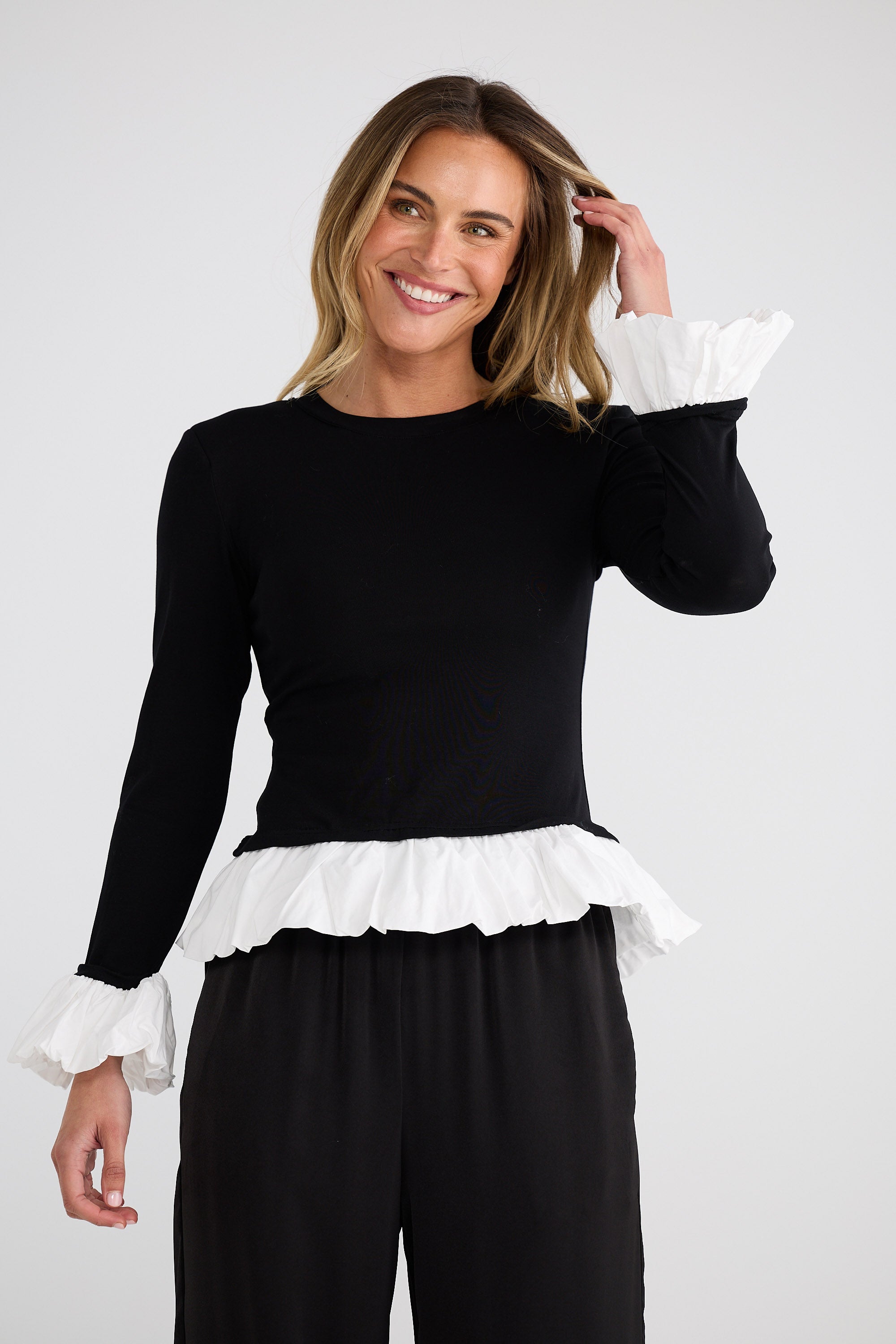 Woman wearing a black top with white ruffled details on a plain background