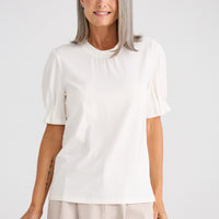 Woman wearing a white blouse with puff sleeves against a plain background
