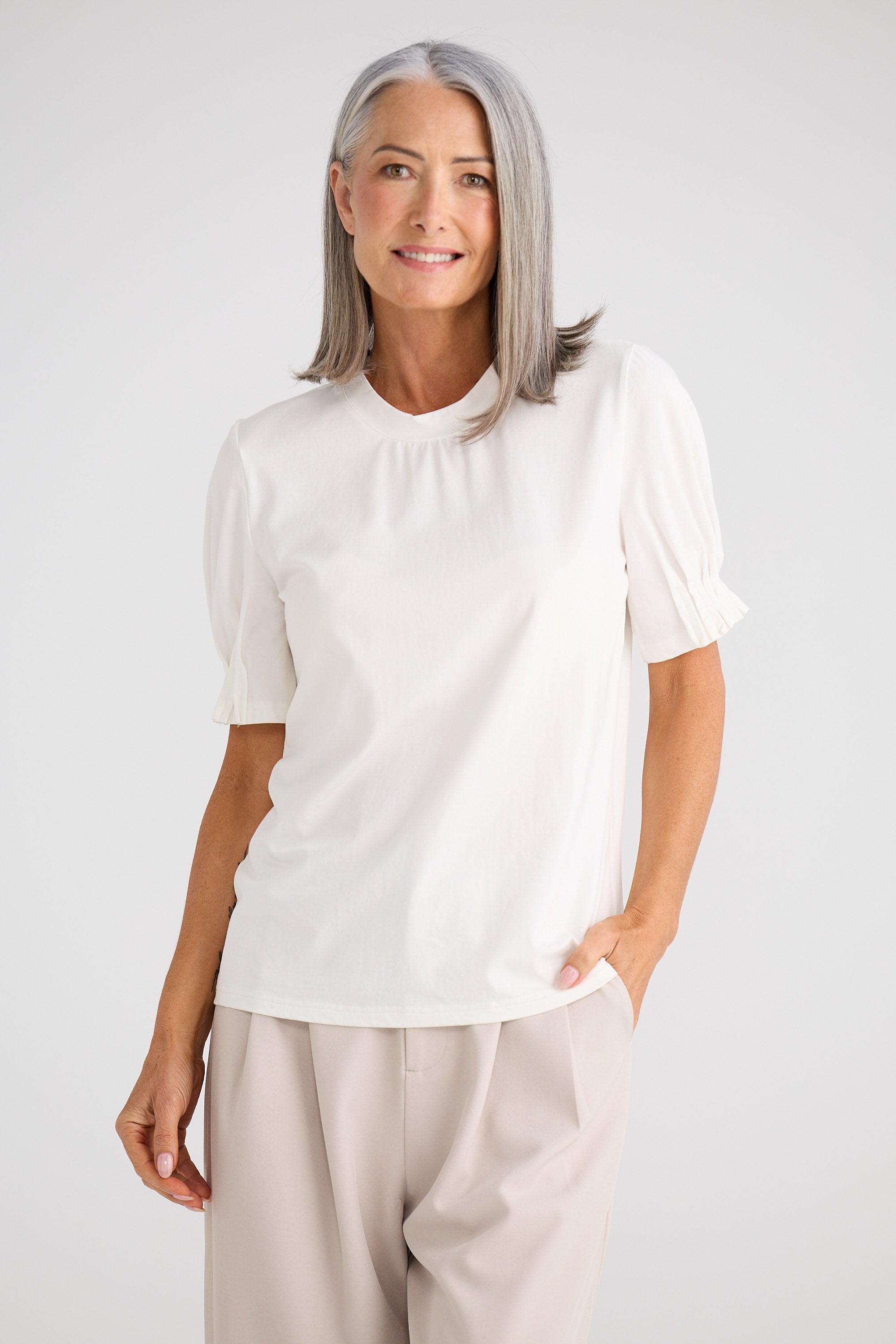 Woman wearing a white blouse and beige pants against a plain background