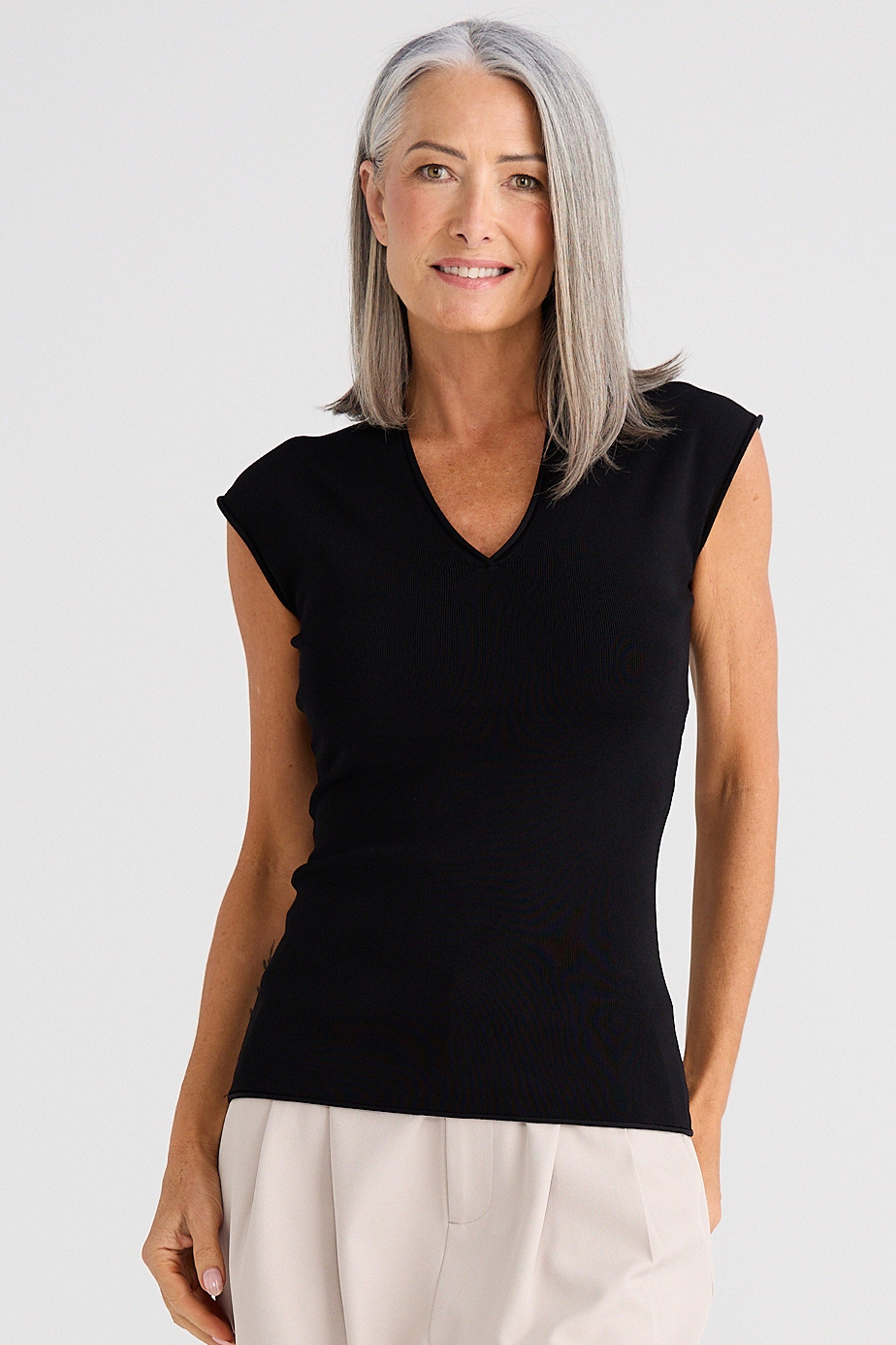 Woman wearing a black sleeveless top and light-colored pants on a white background