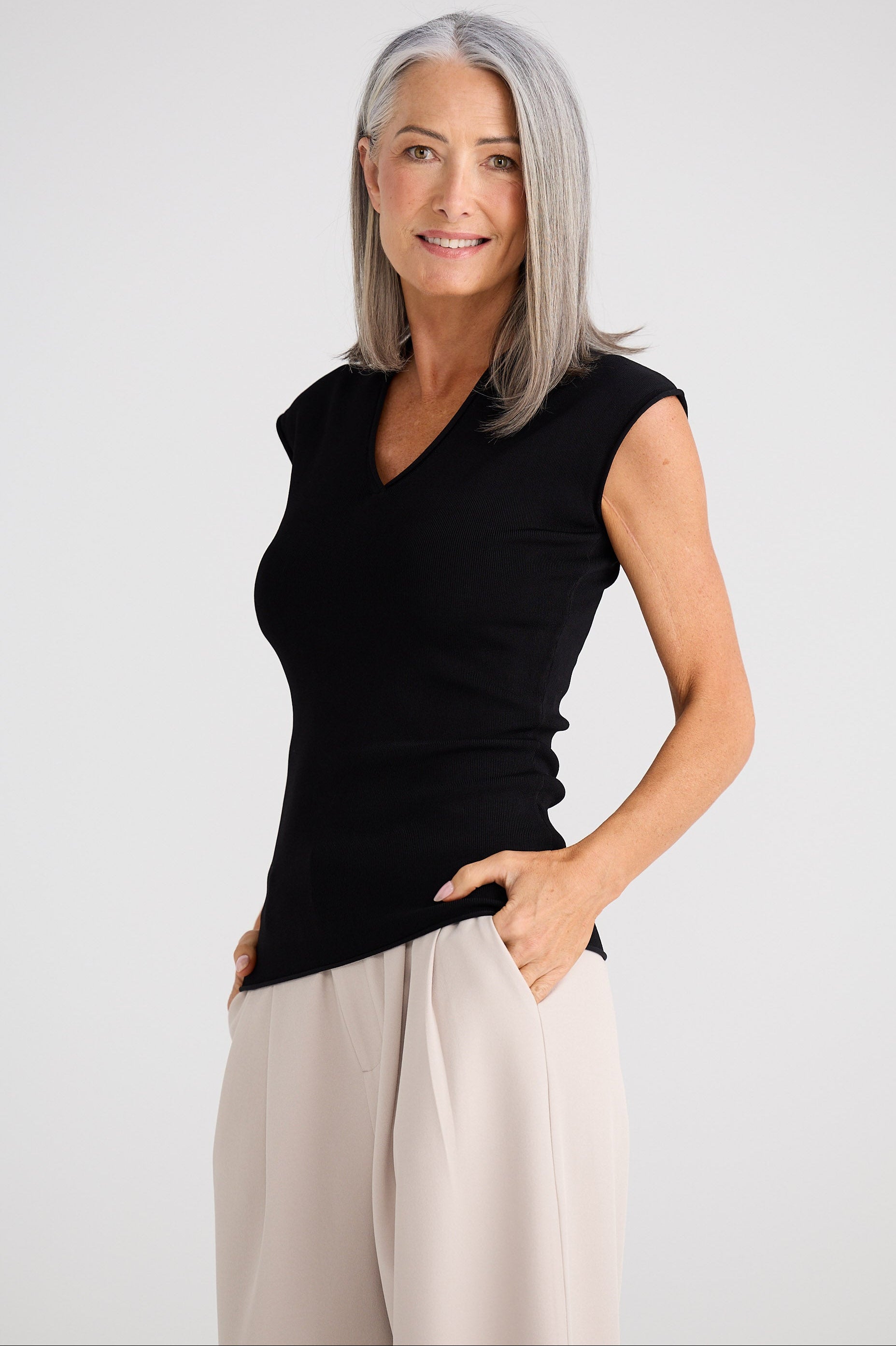 Woman wearing a black sleeveless top and beige pants against a white background