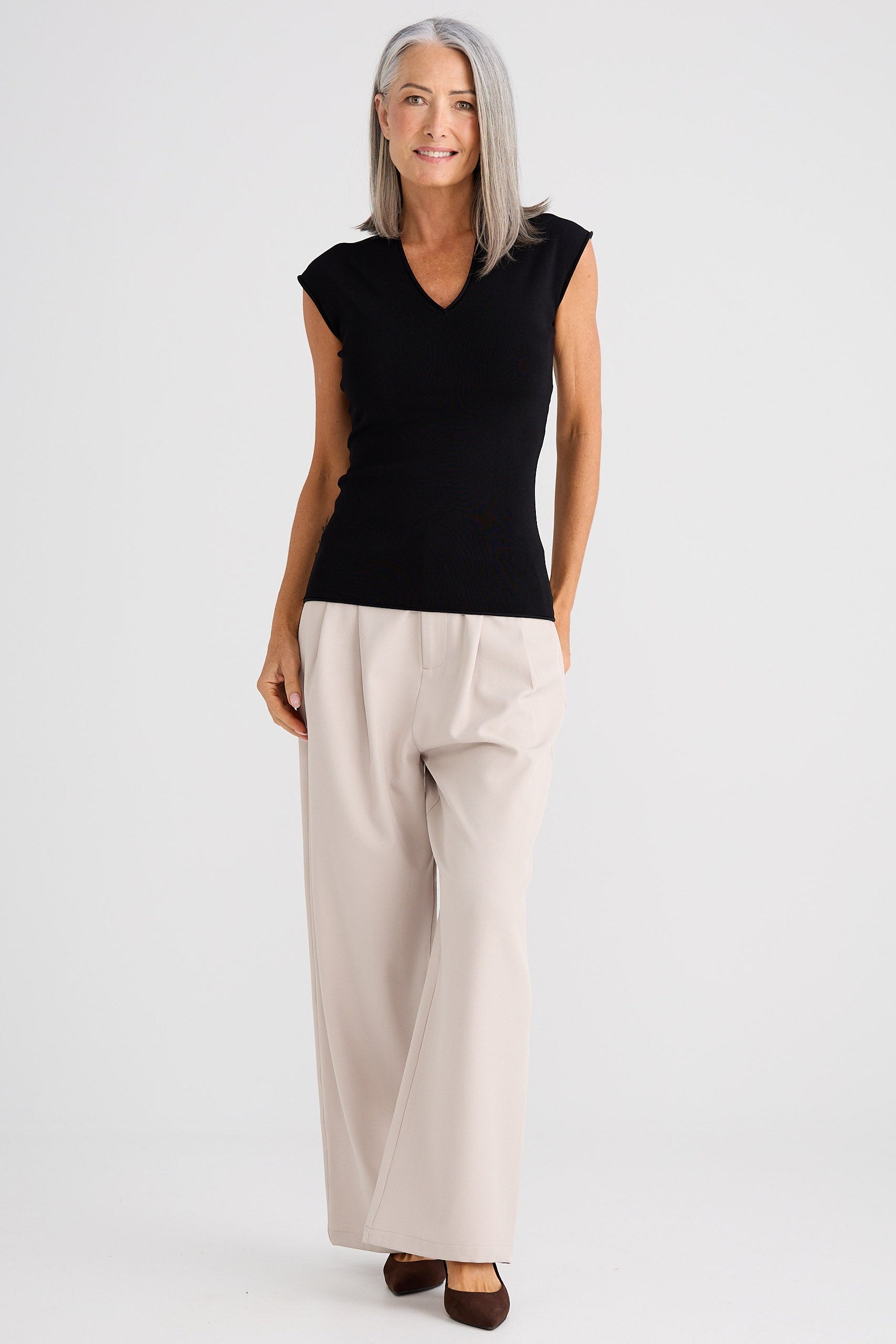 Woman wearing a black sleeveless top and beige pants on a white background